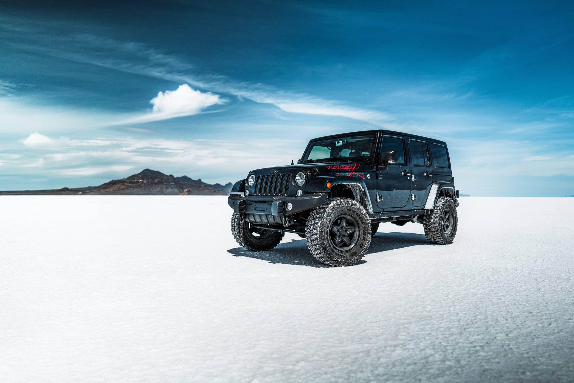黑色Jeep Wrangler停在白色鹽灘上，遠處有山。