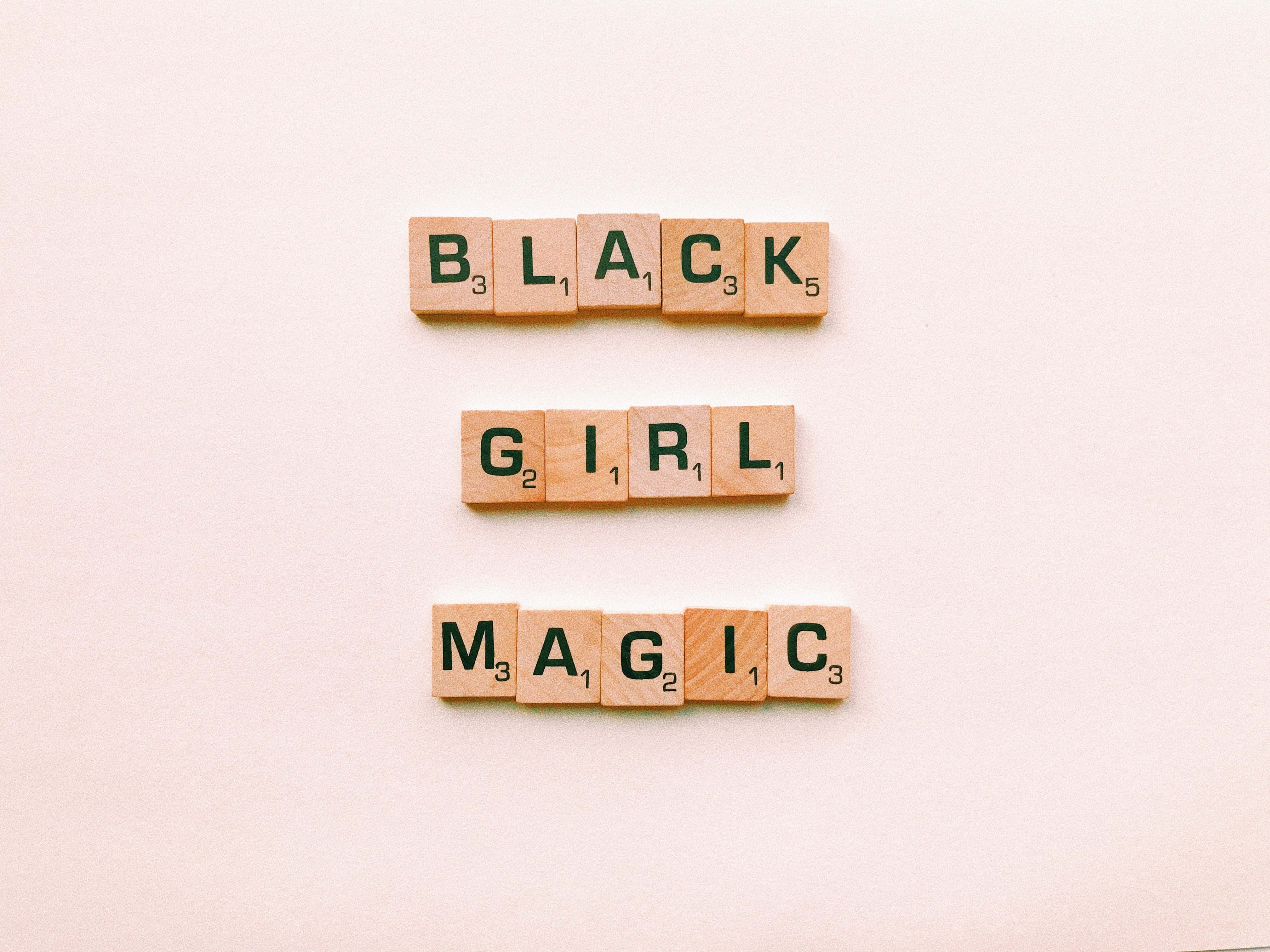黑人女孩魔法拼字遊戲方塊 壁紙 — 木製 Scrabble 字母磚在柔軟的米色背景上用綠色字母拼出「BLACK GIRL MAGIC」。