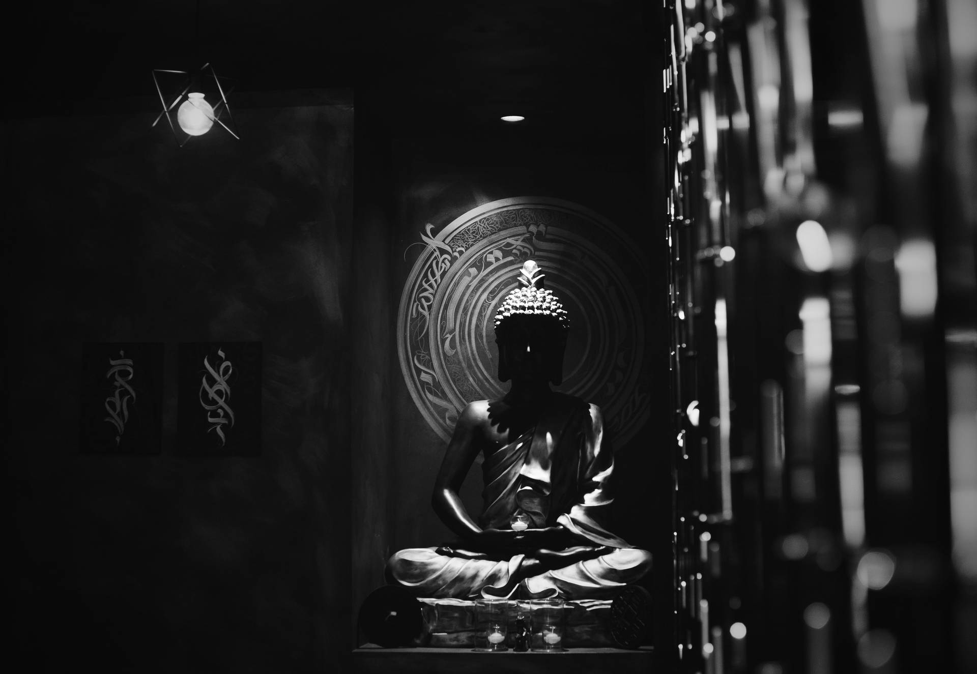 在黑暗簡約的房間中，佛像剪影與曼陀羅牆飾一同冥想。