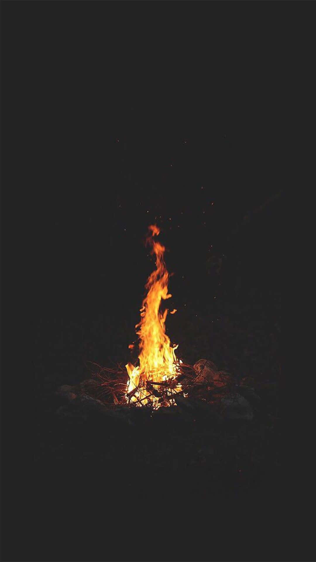 黑夜中燃燒的營火 壁紙 — 一個充滿活力的營火在漆黑的夜空中明亮地燃燒，將溫暖的橙色光芒投射到周圍的岩石上。