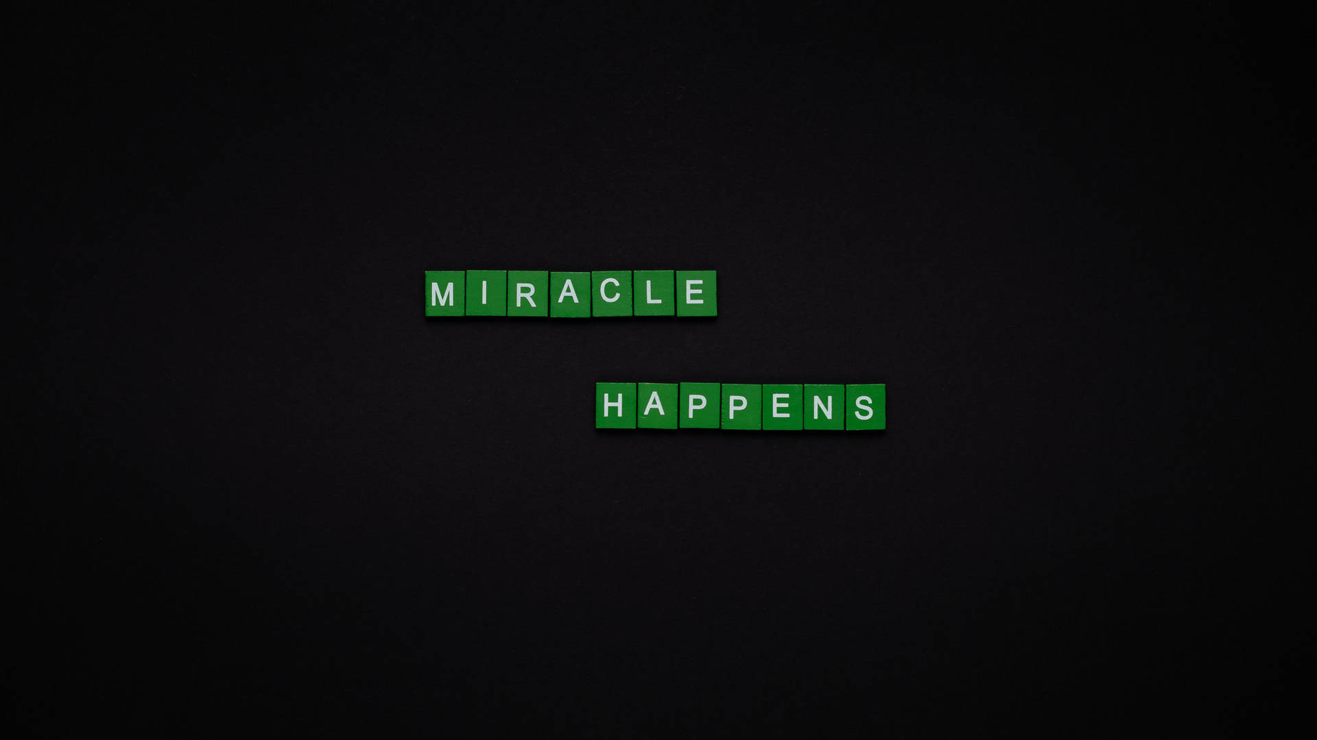 綠色 Scrabble 字母磚在深色背景上拼出 miracle happens。