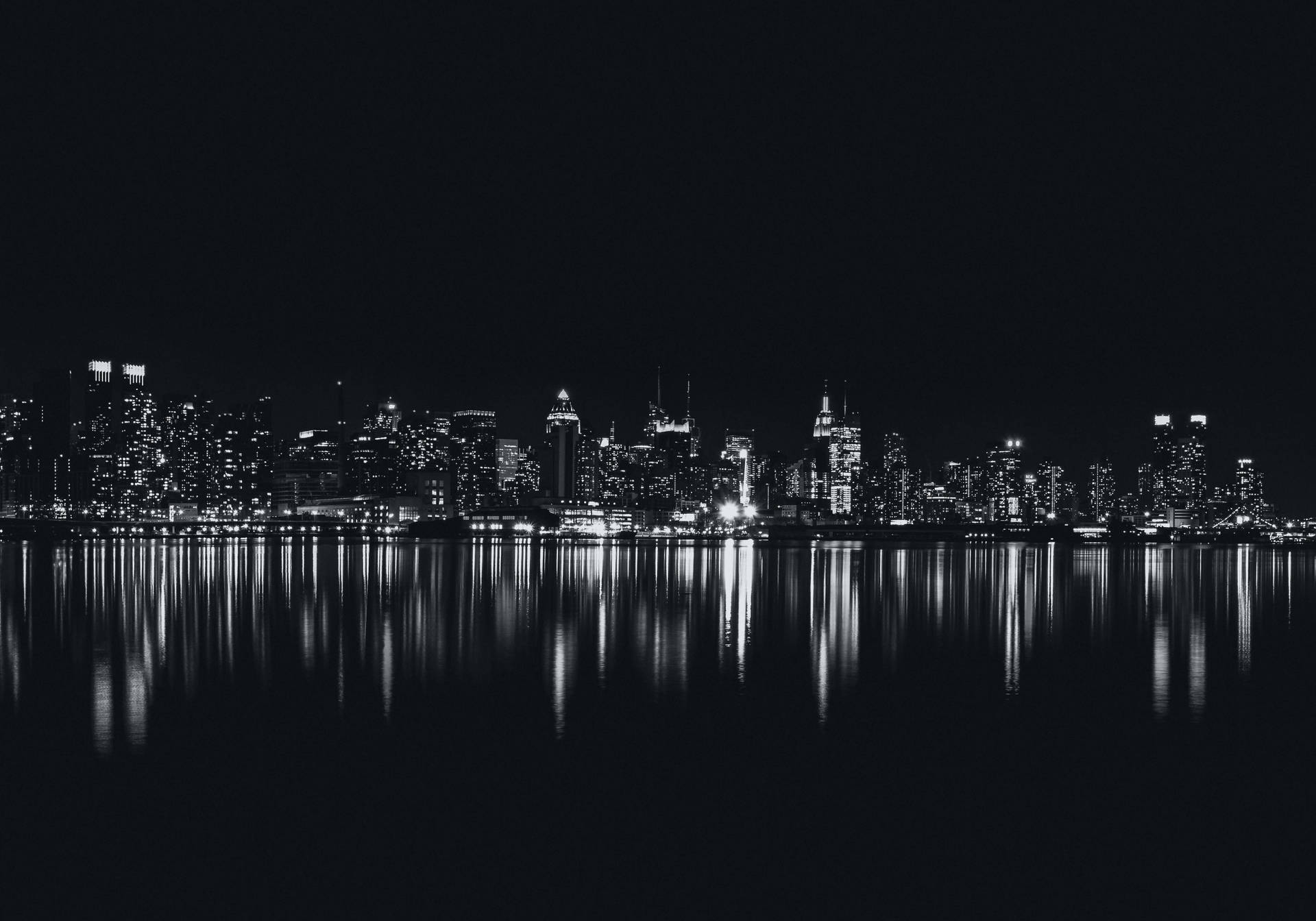 黑白城市天際線倒映在夜晚平靜的水面上。 — 黑屏 壁紙