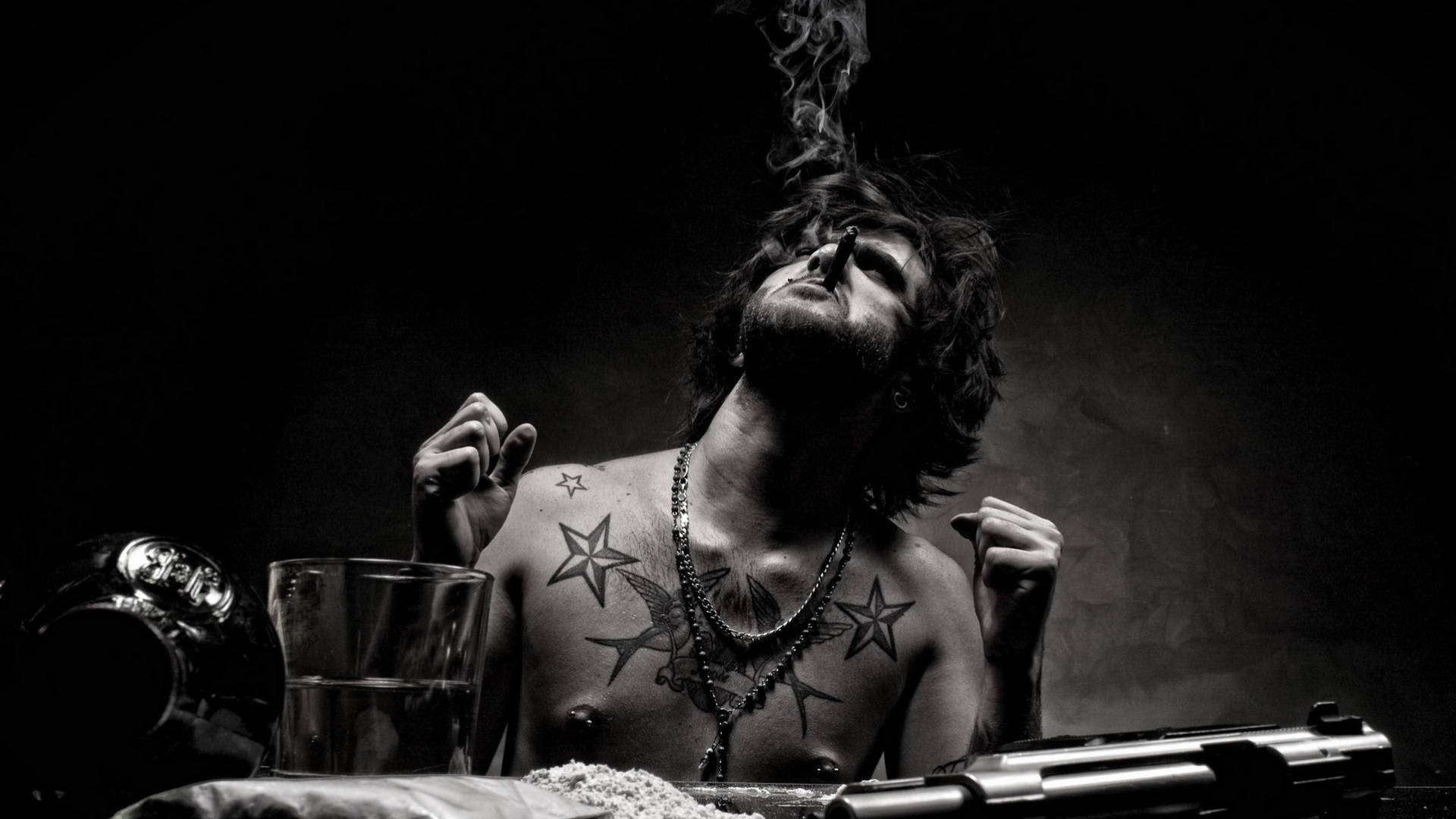 黑幫少年胸前紋身 壁紙 — 一個有紋身的男人在昏暗、陰鬱的黑白場景中，手持香煙向上呼出煙霧。