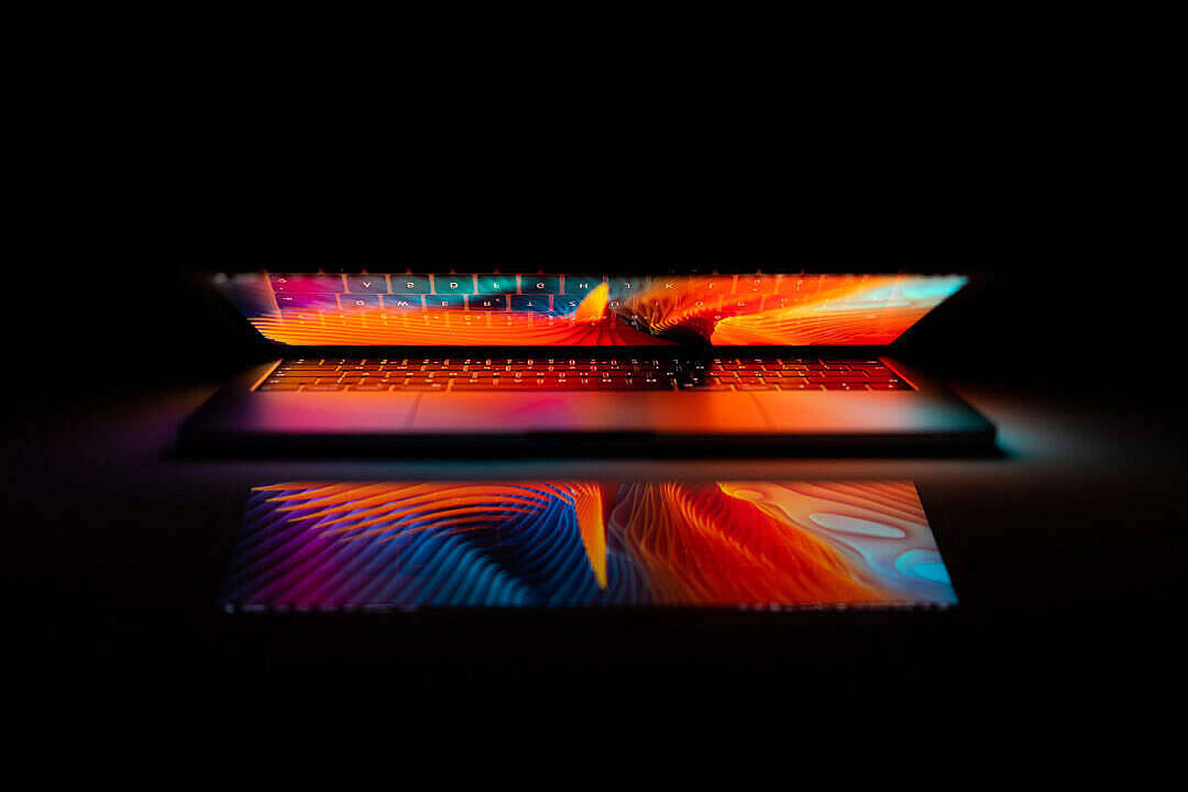 黑暗中亮起的 MacBook Air 2020 壁紙 — 一部時尚筆記型電腦在黑暗背景下，螢幕和鍵盤上散發著充滿活力的抽象波浪光芒。