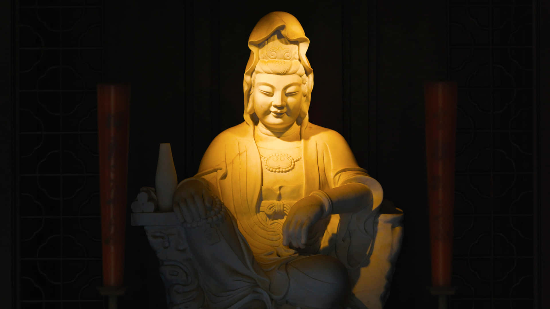一尊柔和照明的佛像，旁邊有蠟燭，在昏暗的房間裡。