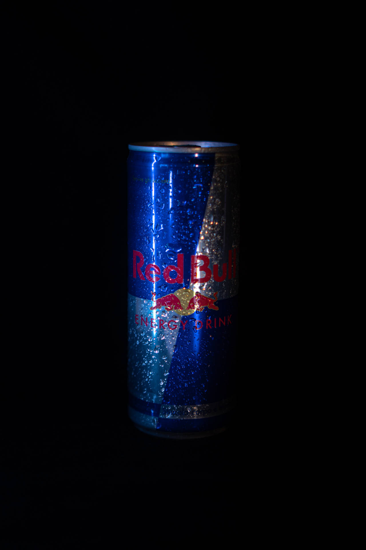 在昏暗的攝影棚燈光下，一個帶有冷凝水珠的冰凍Red Bull罐。
