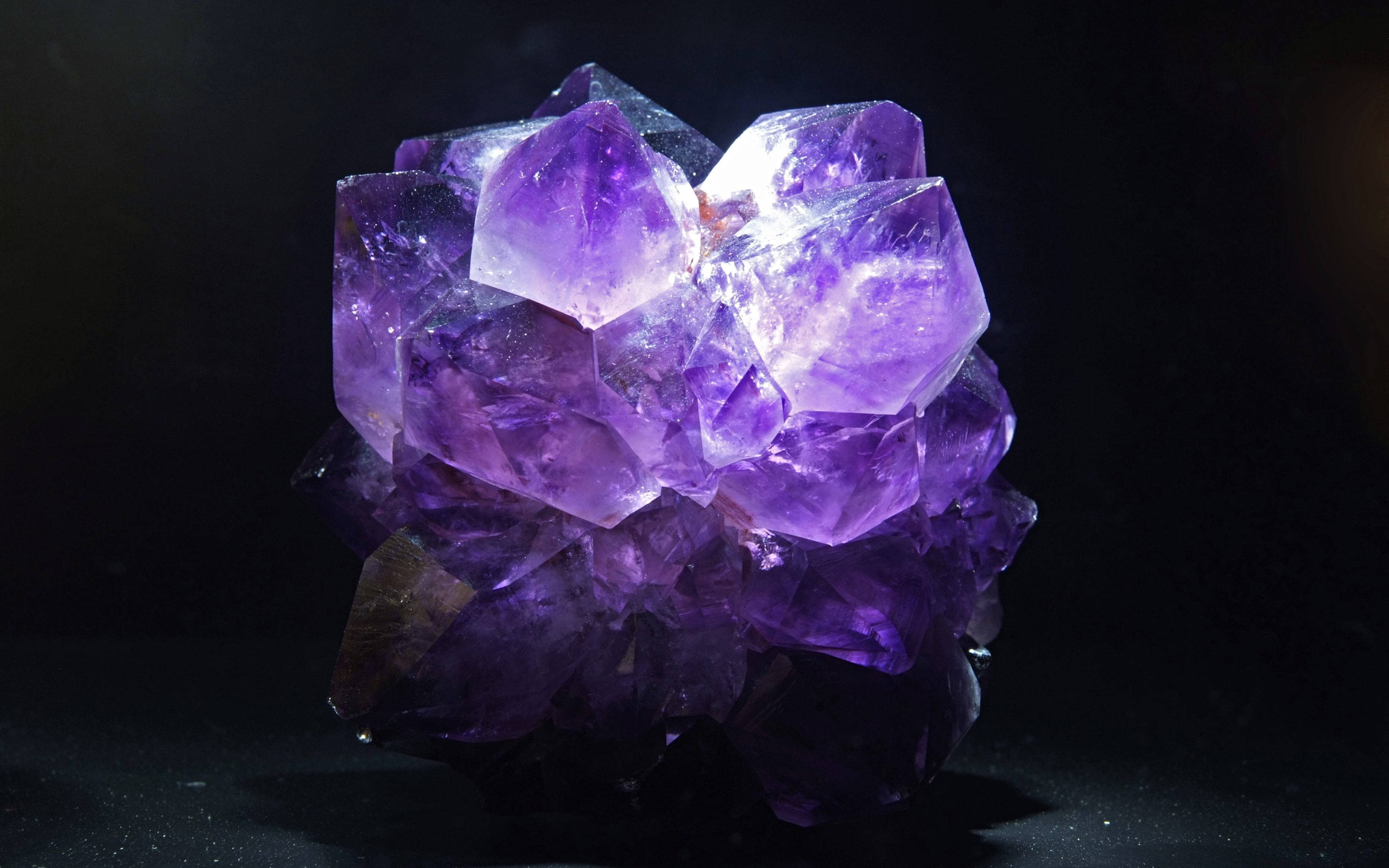 黑暗中的紫水晶 壁紙 — 一簇閃耀的紫色紫水晶晶體在深黑色背景下發出內在光芒。