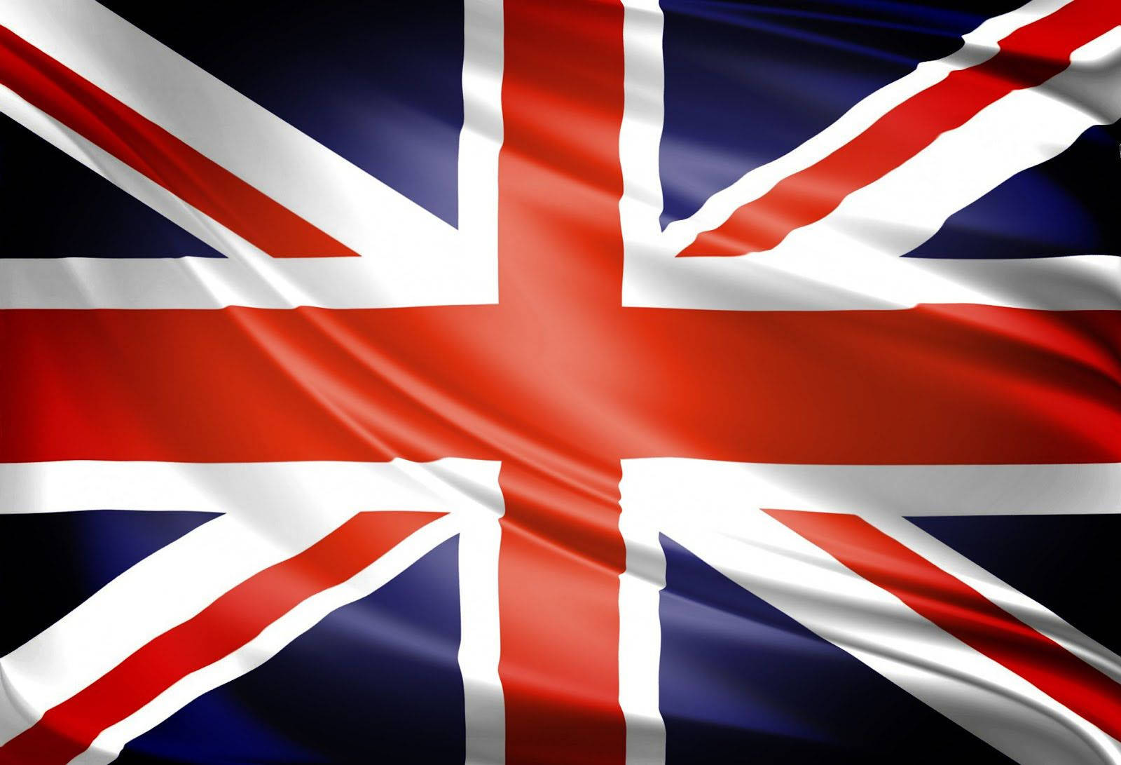 黑暗場景中的英國國旗 壁紙 — 英國國旗在明亮的日光下以豐富的紅色、白色和深藍色動態飄揚。
