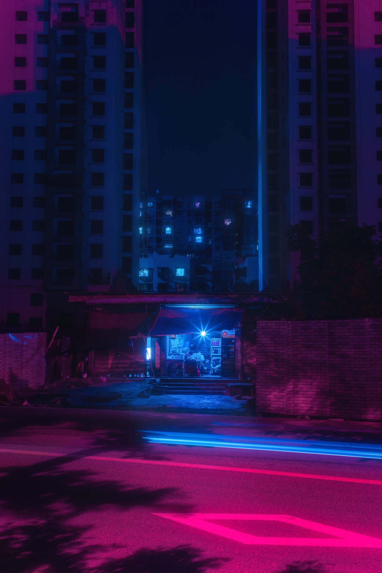 霓虹粉紅和藍色光跡在夜間照亮高樓之間的潮濕城市街道。