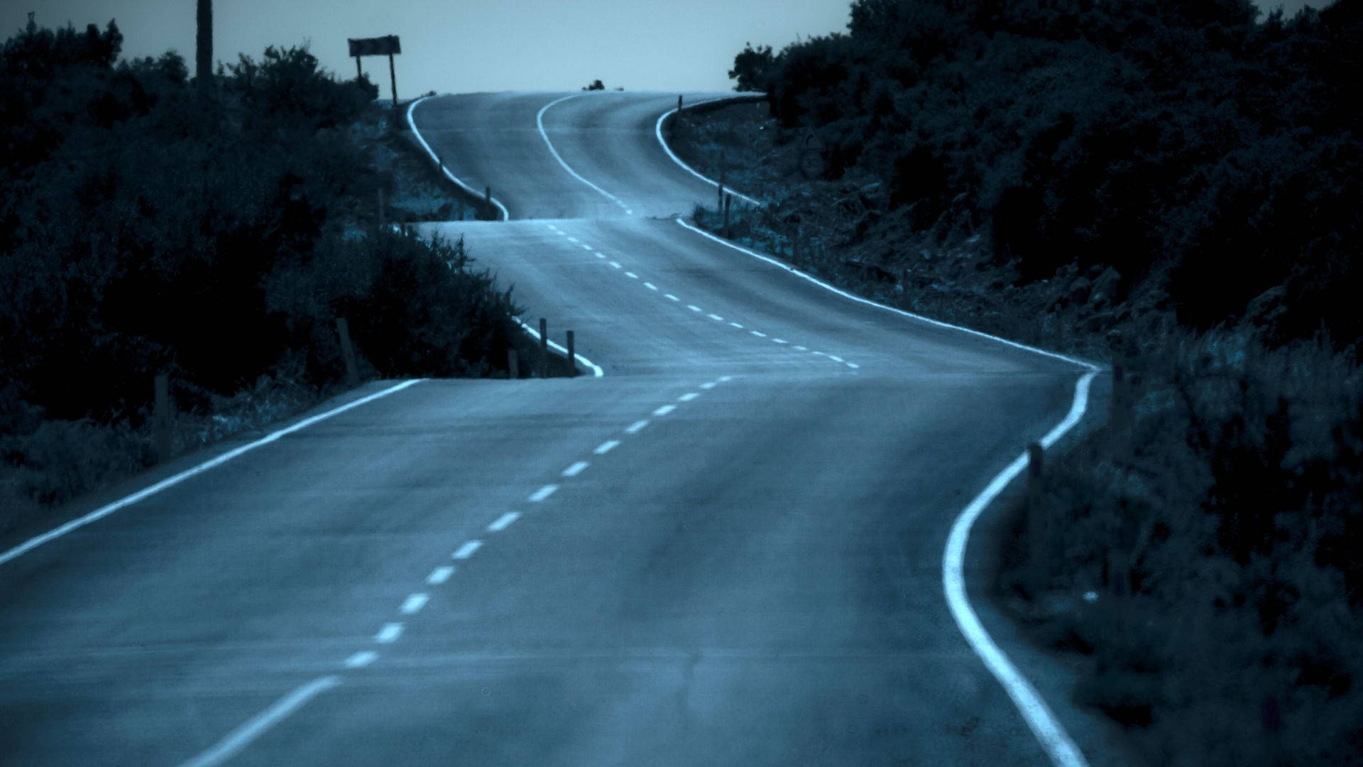 黑暗彎曲長路之旅 壁紙 — 一條蜿蜒的道路在暮色天空下彎曲進入迷霧遠方，兩旁是黑暗的灌木叢和發光的白色線條。