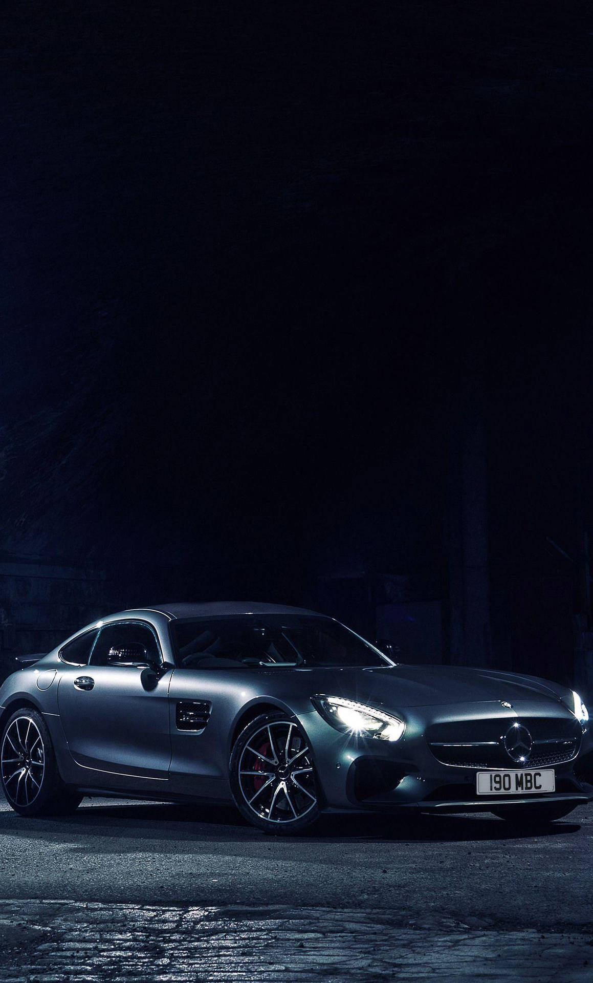 銀色 Mercedes-AMG GT 跑車在黑暗鵝卵石街道上被車頭燈照亮。