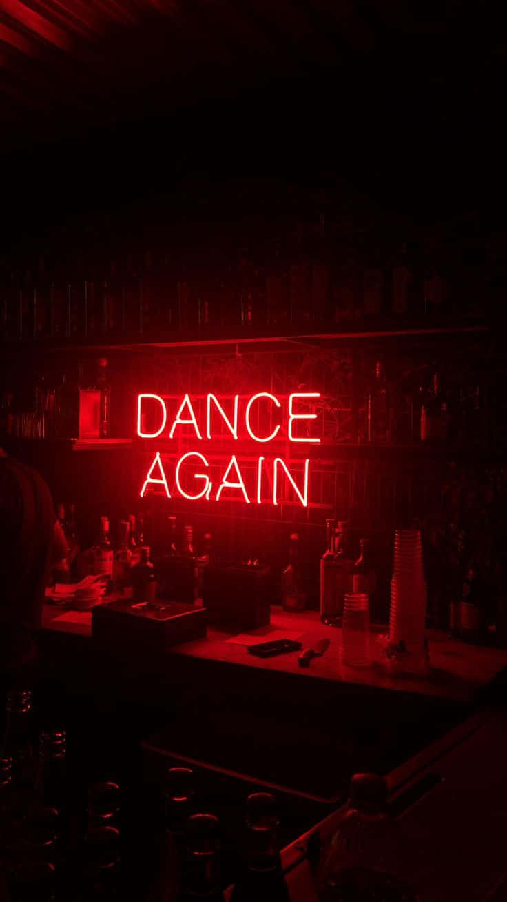 在昏暗的酒吧中，一個紅色霓虹燈牌寫著 dance again，旁邊有酒瓶和酒杯。