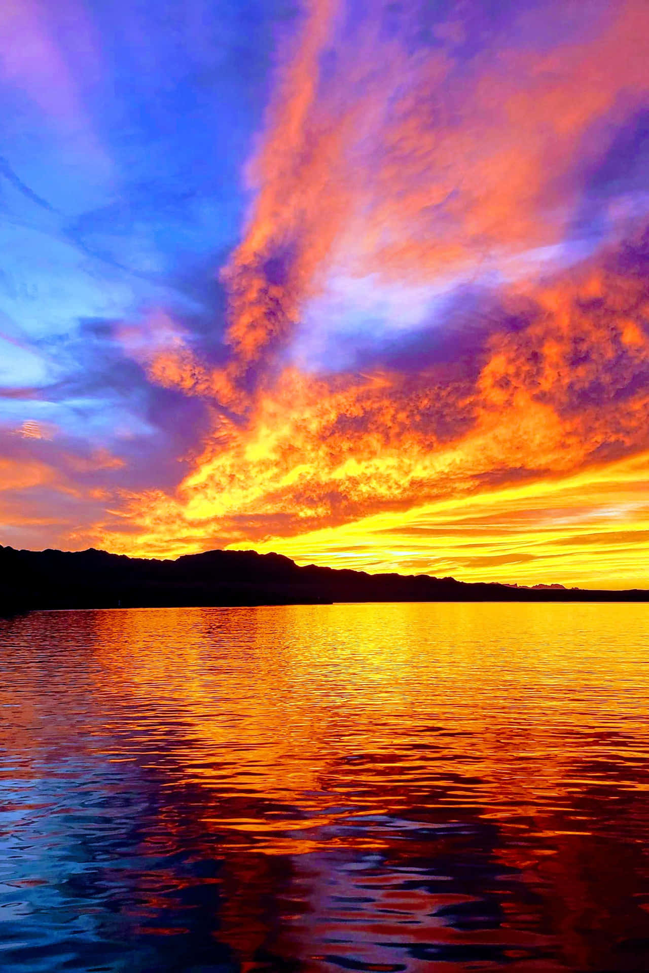 鮮豔的夕陽色彩倒映在平靜的湖面上，山巒呈現剪影。