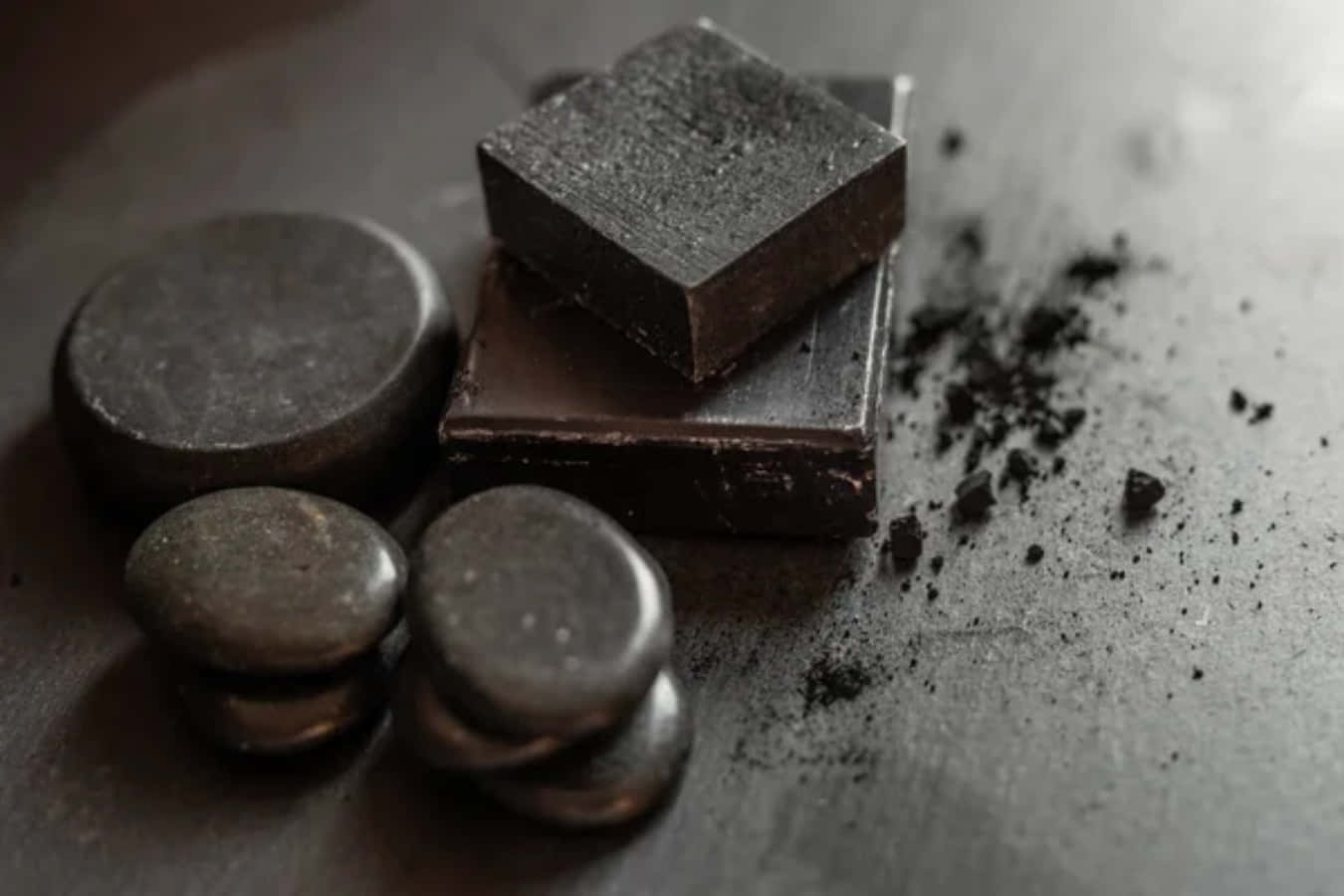 Black Soap 桌布 壁紙 — 黑朱古力條和光滑的石頭放在帶有碎屑的紋理灰色表面上。