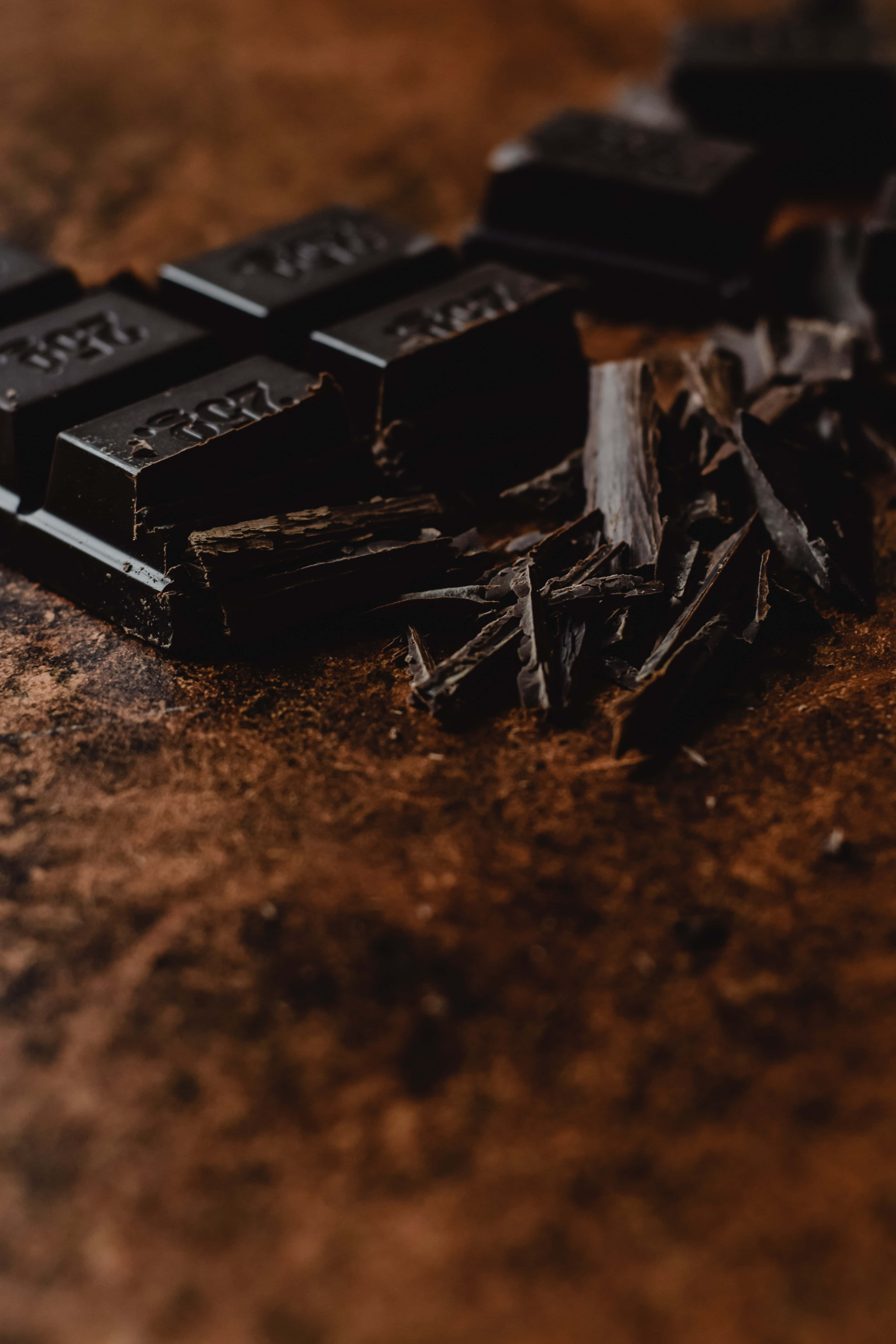Dark Chocolate 桌布 壁紙 — 黑朱古力條和碎塊特寫，放置在濃郁的棕色可可粉表面上。