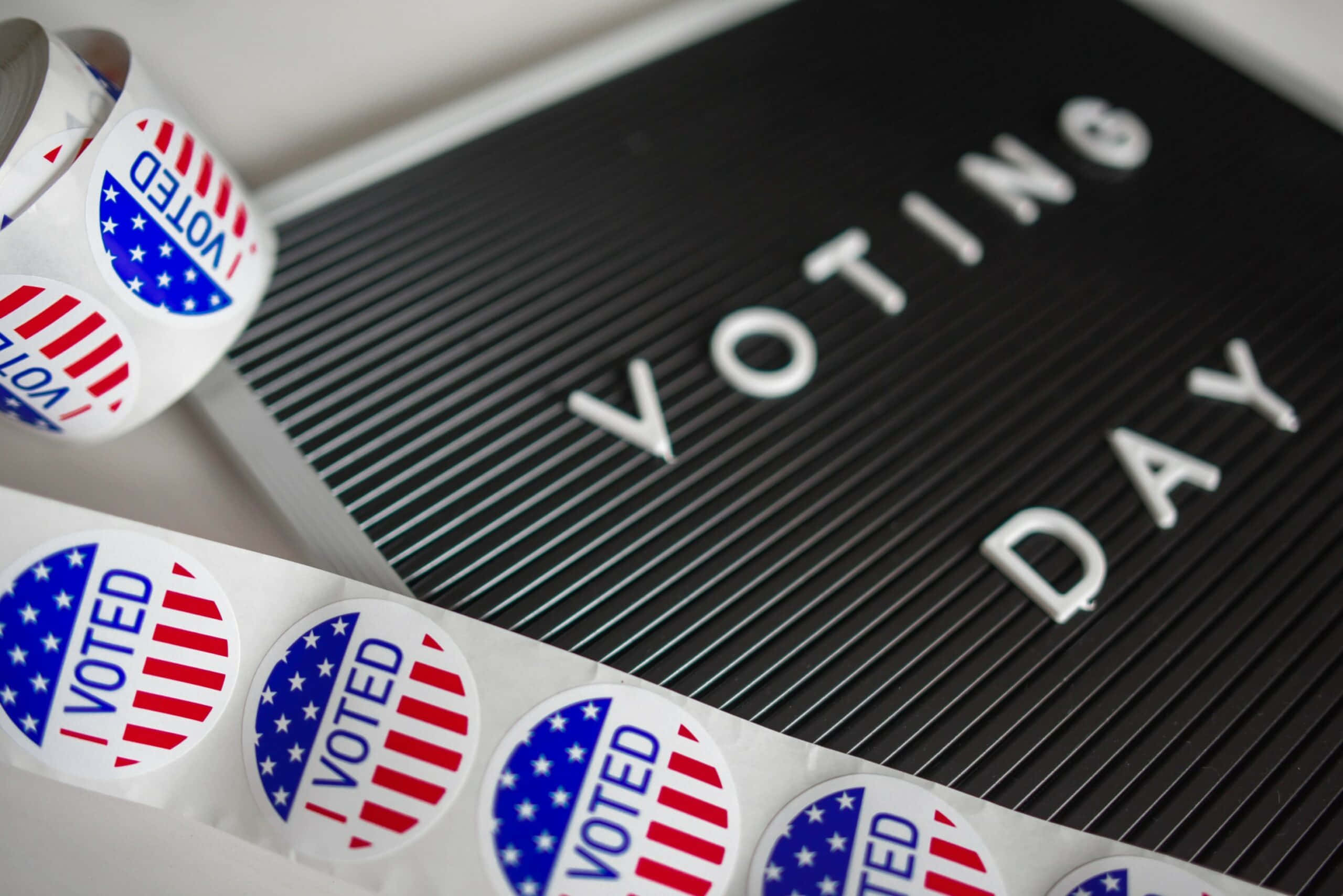 Election 桌布 壁紙 — 黑板上的「VOTING DAY」字母瓷磚旁邊放著愛國「I VOTED」貼紙卷的特寫。