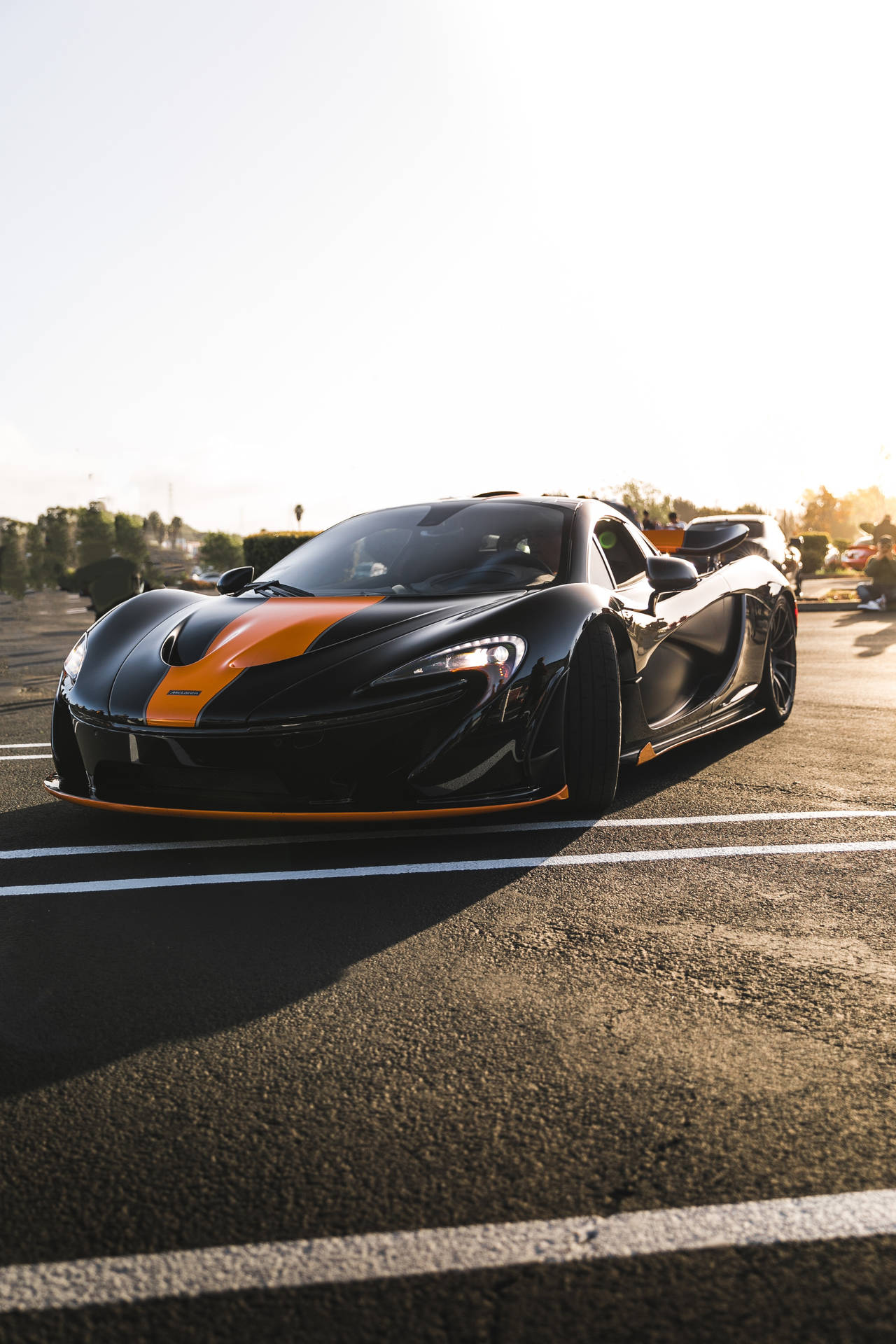 黑色McLaren跑車帶有橙色條紋，停在瀝青路上，夕陽西下。