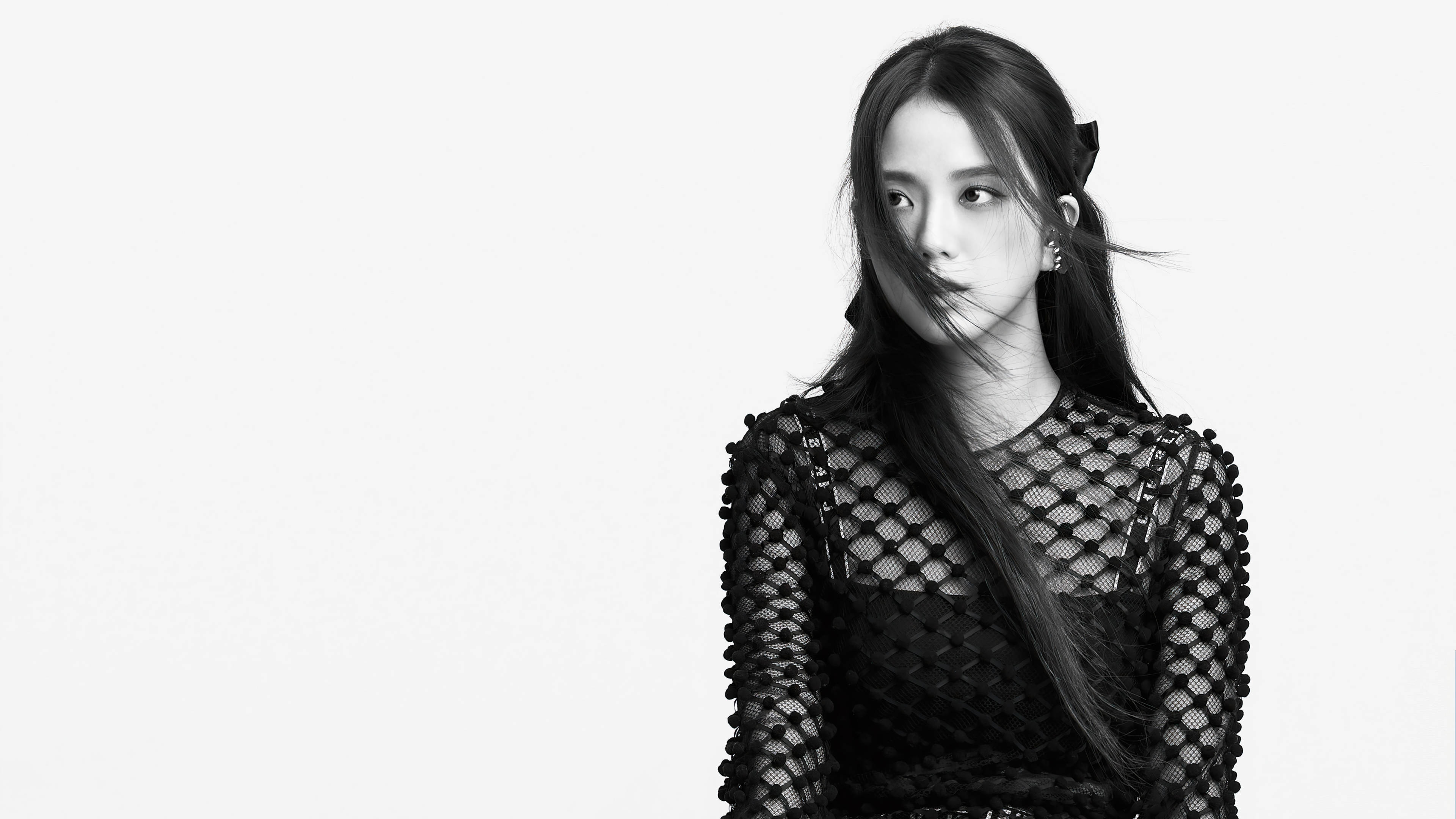 黑白Jisoo 壁紙 — 一個黑白肖像，一位穿著魚網上衣、頭髮被風吹拂的女性，背景是純白色。