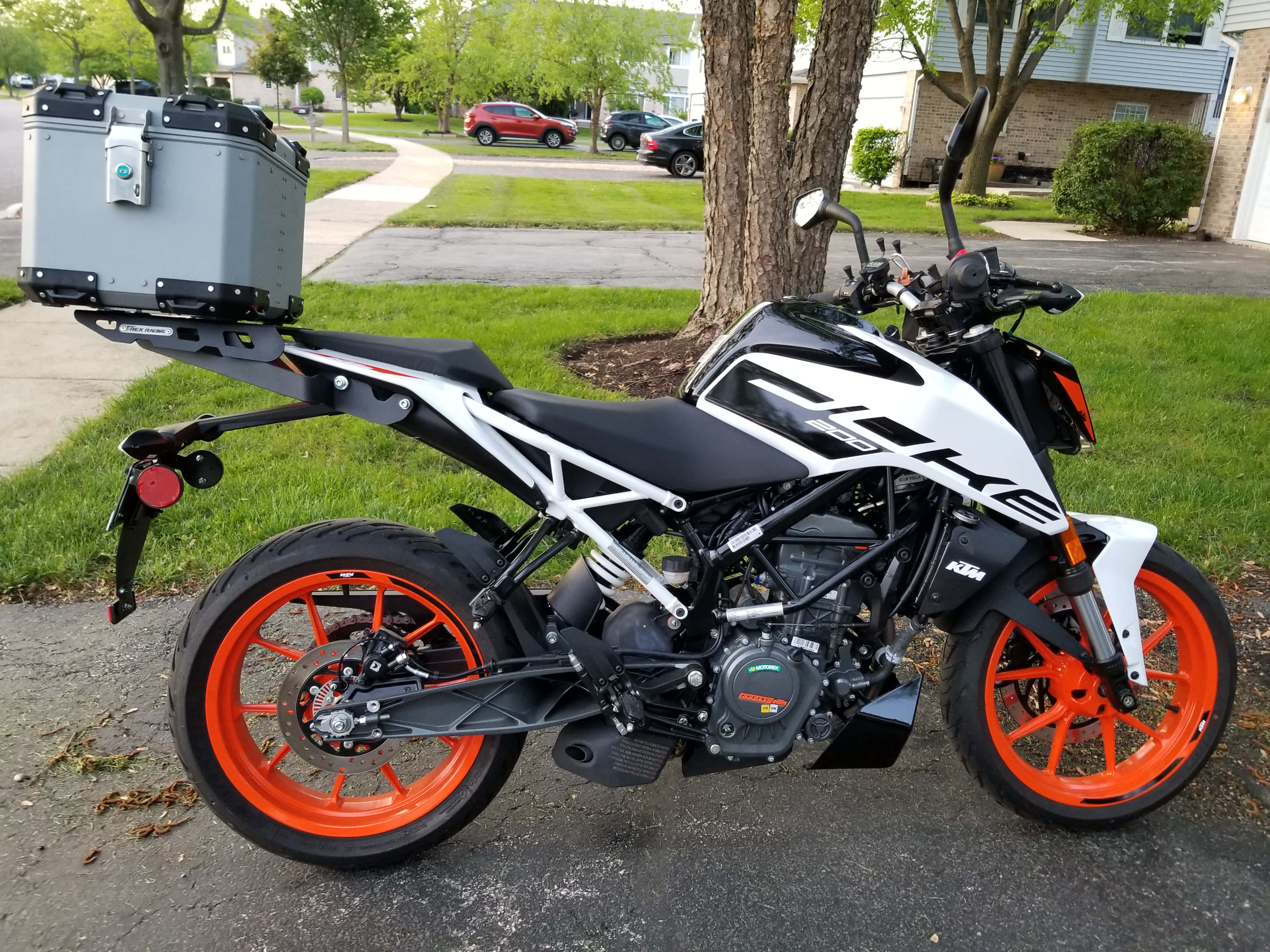 黑白KTM Duke 390圖片 壁紙 — 一架白色和黑色的KTM電單車，帶有亮橙色輪胎，停泊在郊區街道旁的一棵樹旁邊。