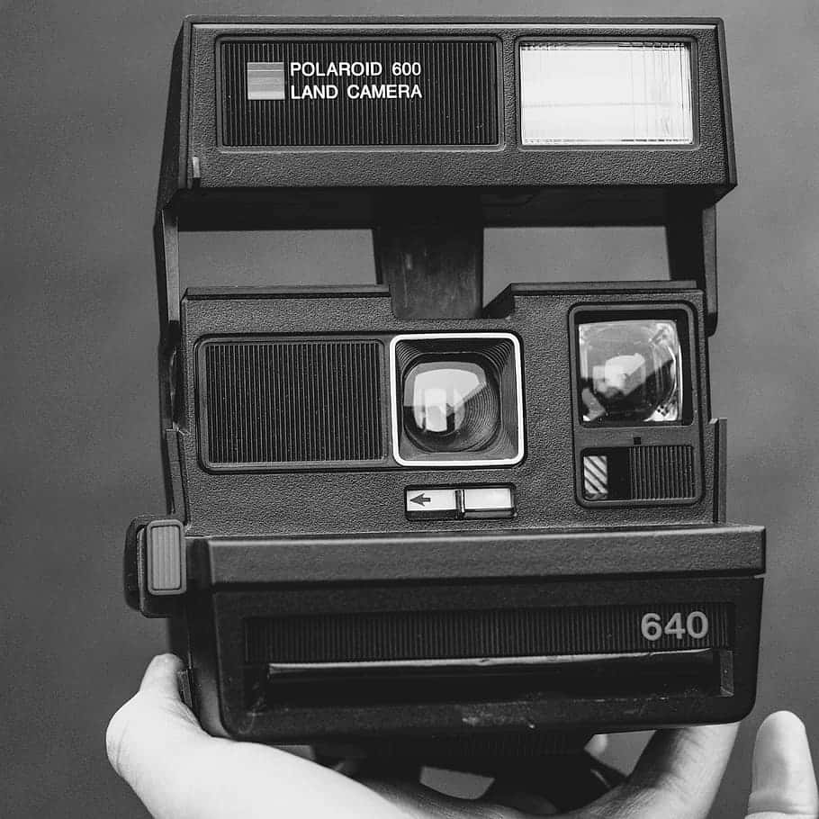 一隻手拿著一部黑白復古Polaroid 600 Land相機。