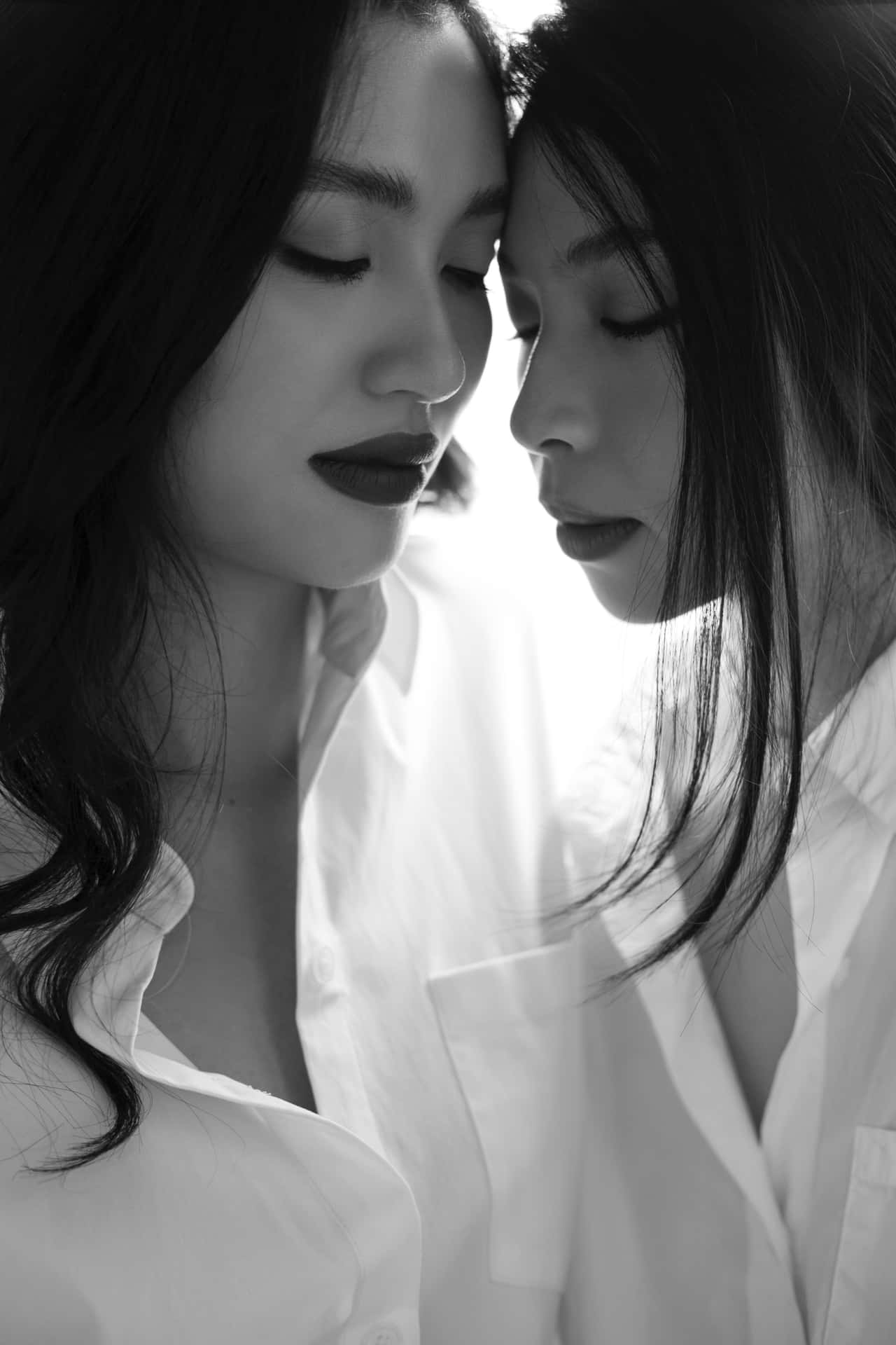 兩位身穿白恤衫的女性額頭相觸的黑白肖像照。