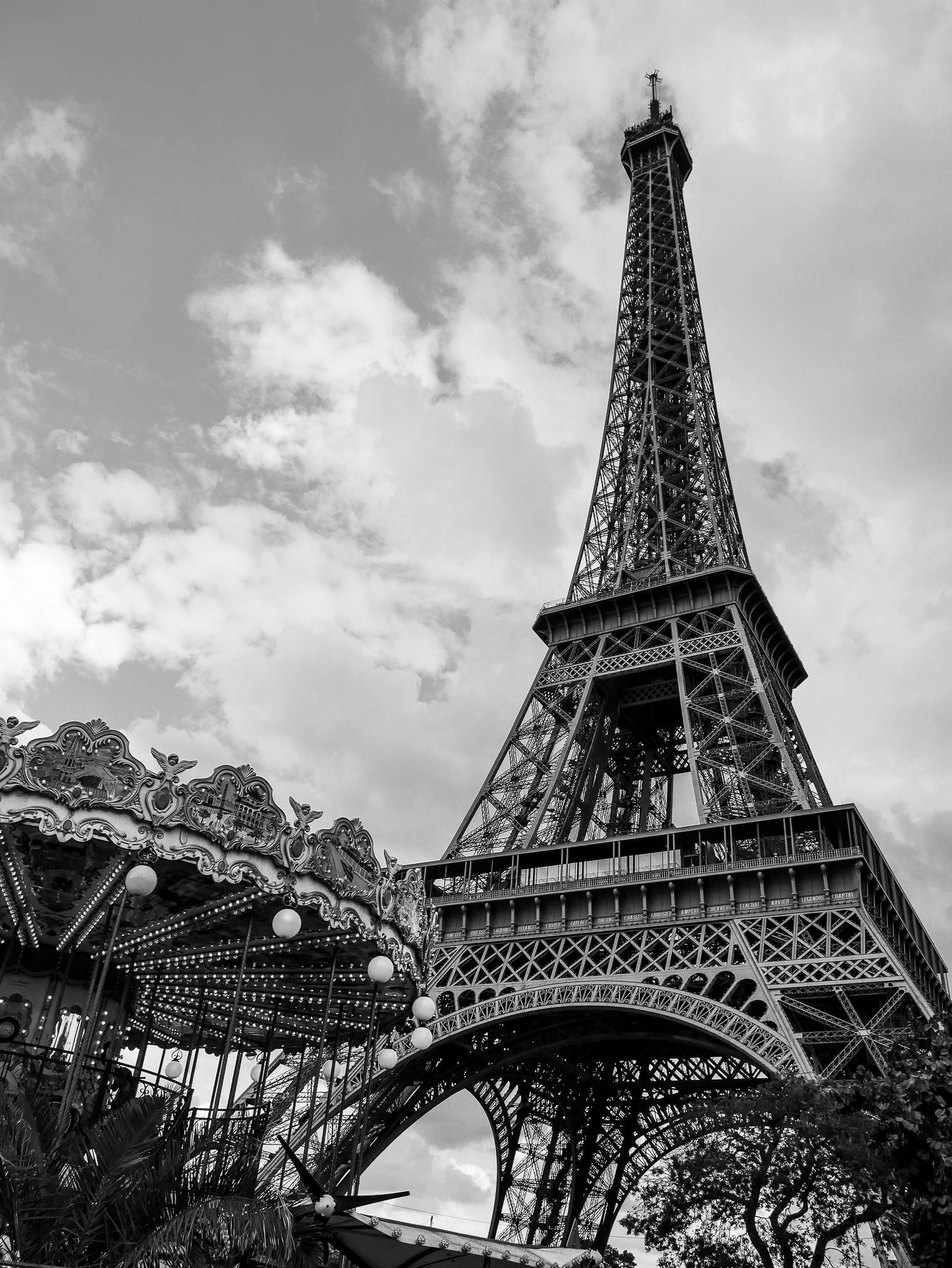 Eiffel Tower 桌布 壁紙 — 黑白低角度拍攝的艾菲爾鐵塔，聳立在華麗旋轉木馬之上，天空多雲。