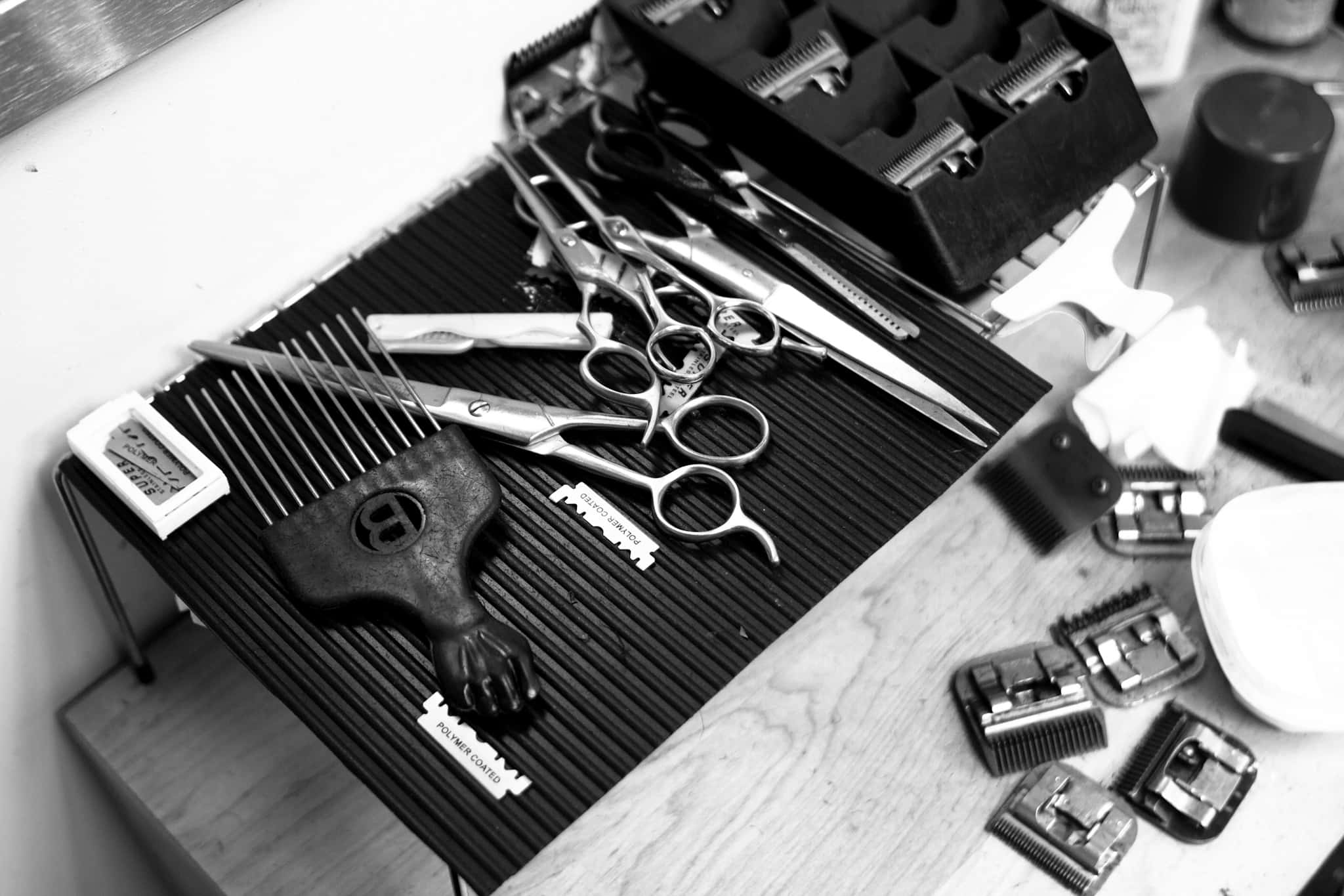 Haircare 桌布 壁紙 — 黑白俯拍照片，展示放在條紋墊上的理髮工具，包括剪刀、推剪和梳子。