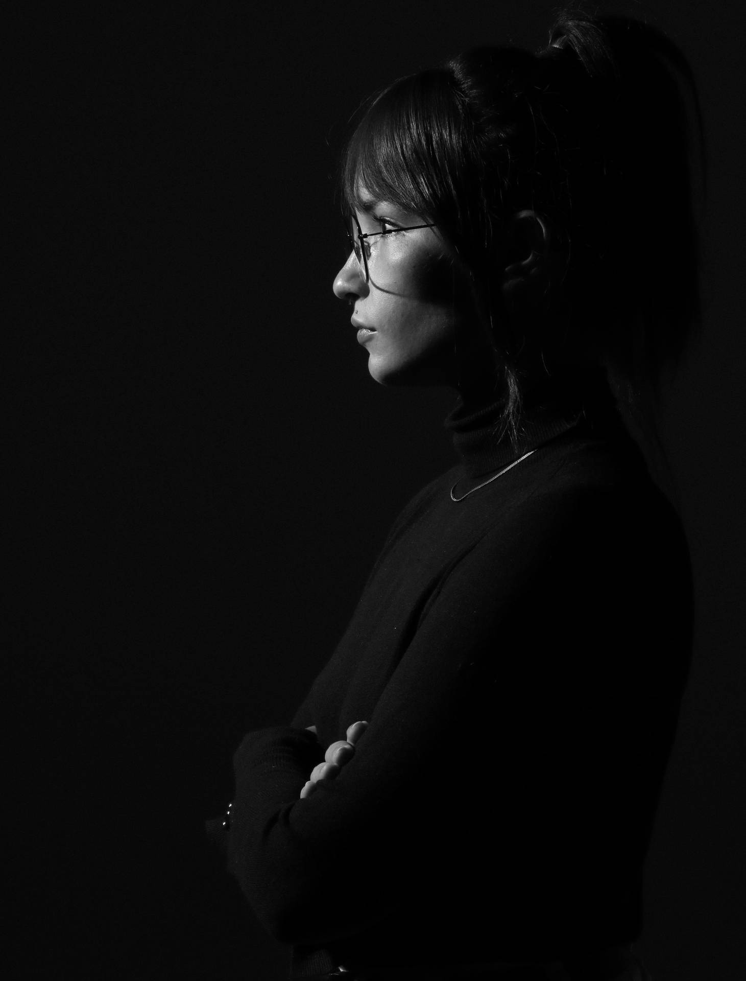 戴眼鏡、雙臂交叉的女性側面黑白攝影棚照。