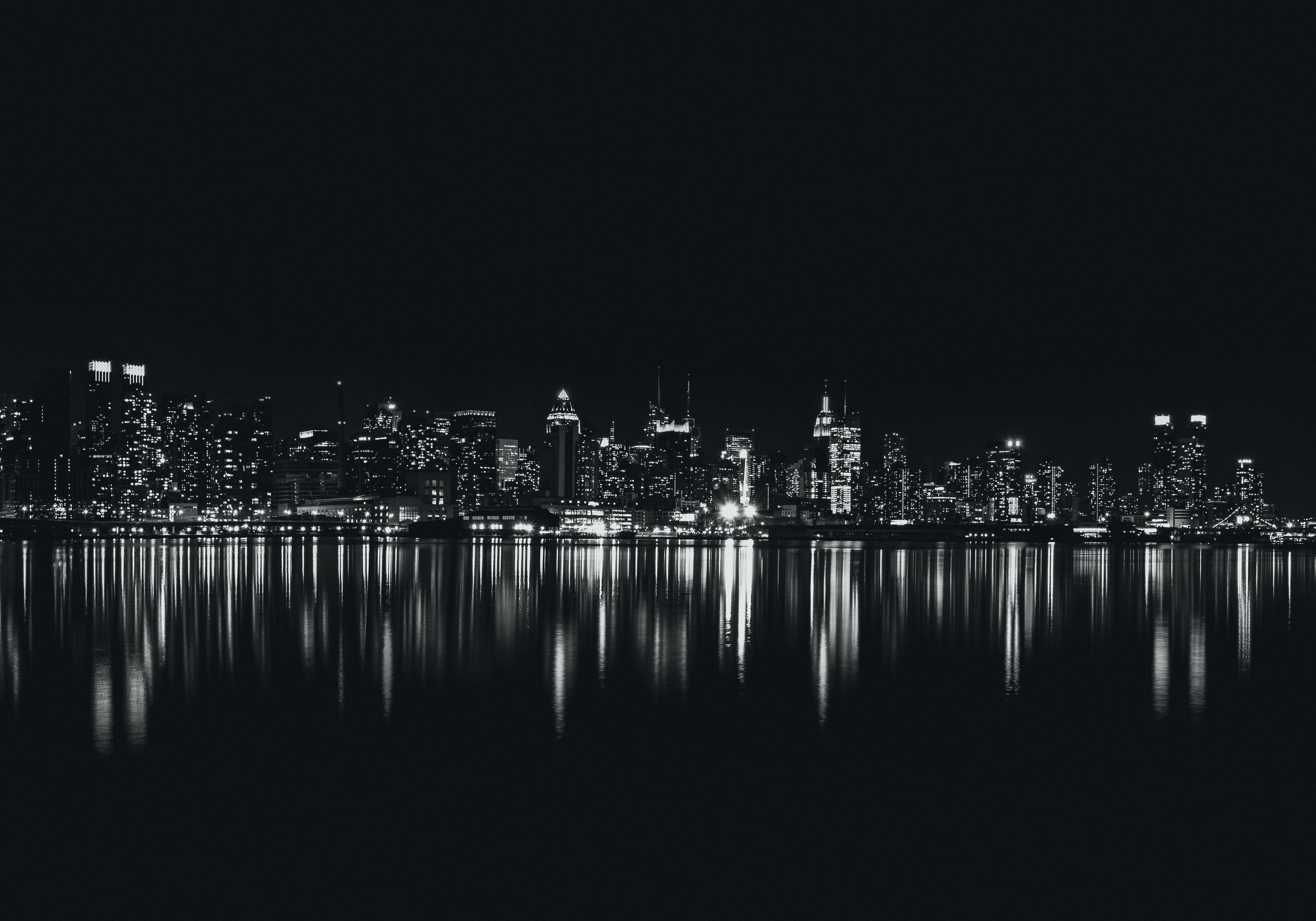 黑白城市風景 4K 桌面 壁紙 — 夜晚單色城市天際線，發光的窗戶完美倒映在平靜的水面上。