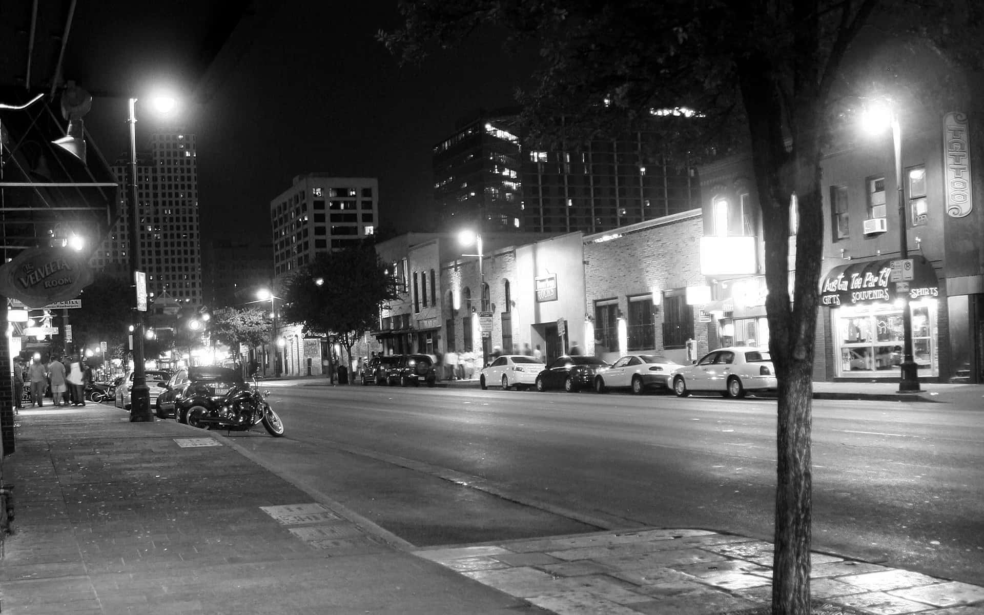 Night Street 桌布 壁紙 — 黑白夜景城市街道場景，有停泊的汽車、發光的街燈和行人路上的行人。