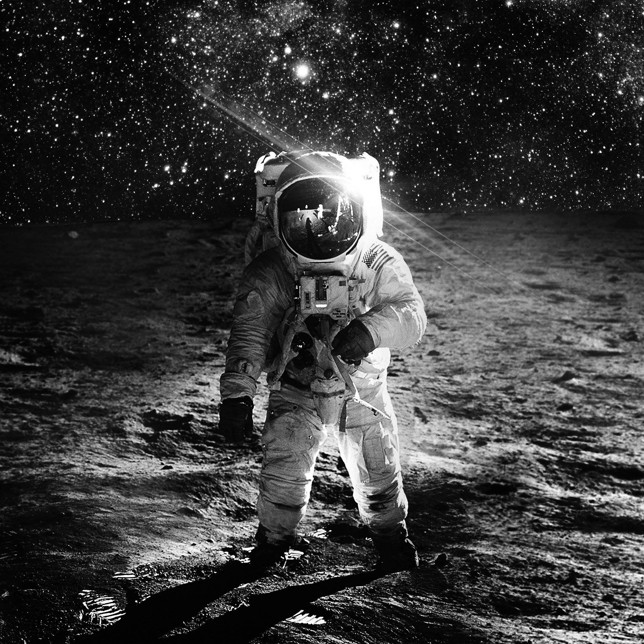 黑白太空宇航員 壁紙 — 太空人站在月球表面，星空下，頭盔反射地球，明亮的陽光投下長長的影子。