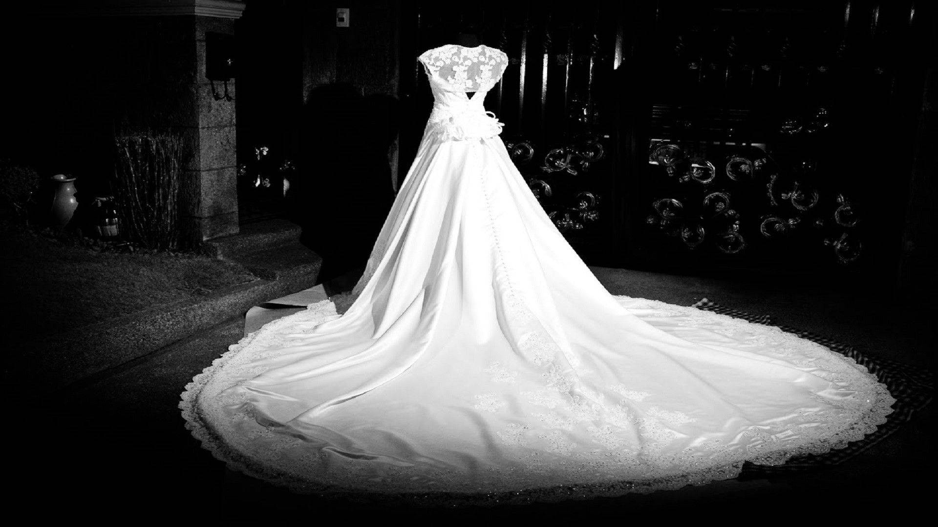 黑白婚紗 壁紙 — 一件令人驚嘆的白色婚紗，帶有蕾絲細節和豐盈的裙擺，在夜間戲劇性地照亮在黑暗華麗的門口前。