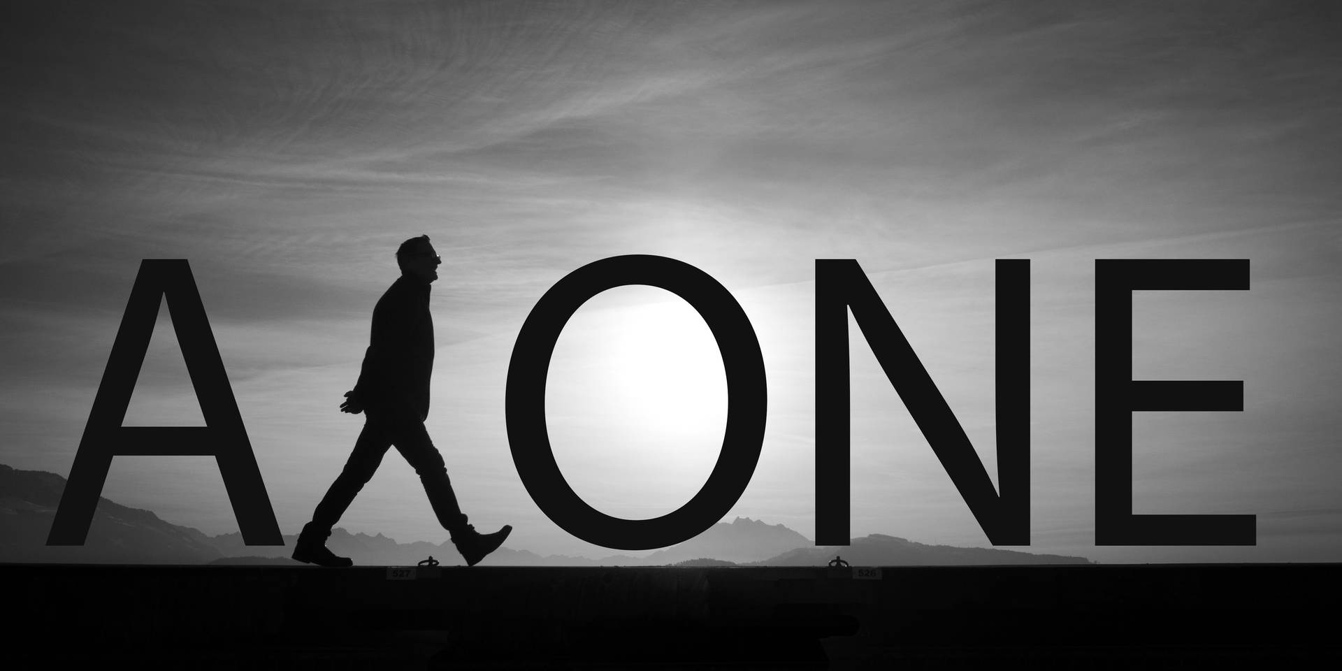 一個人走過拼出「ALONE」的巨大字母，背景是灰色天空。