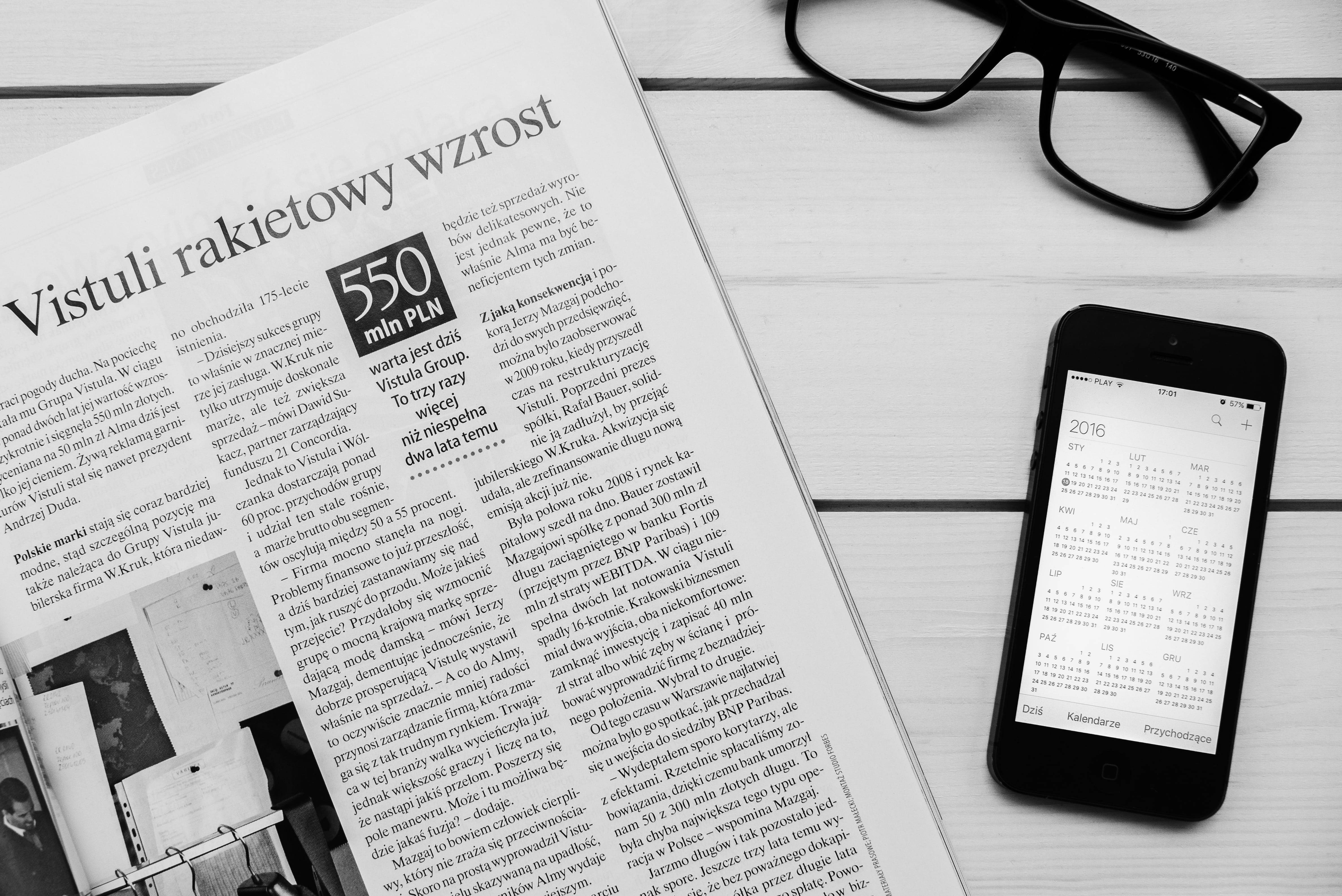 Newspaper 桌布 壁紙 — 黑白平鋪構圖：報紙文章、眼鏡及顯示日曆的智能手機置於木質表面上。