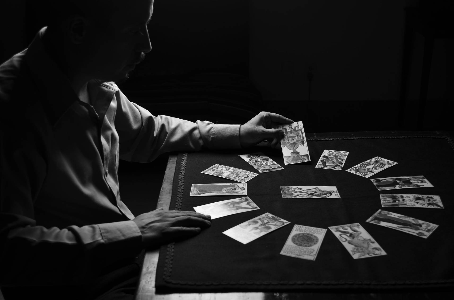 在昏暗光線中，一個人手持塔羅牌，放在桌上攤開的牌陣上方。