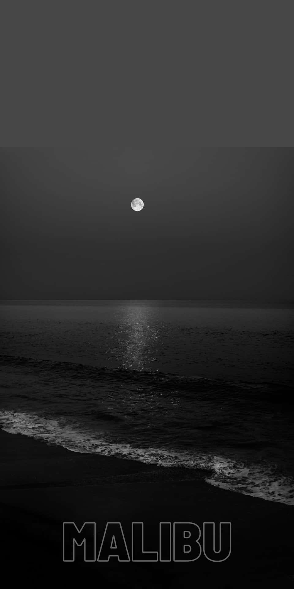 滿月照在黑暗的海洋上，在夜間海灘的水面上反射