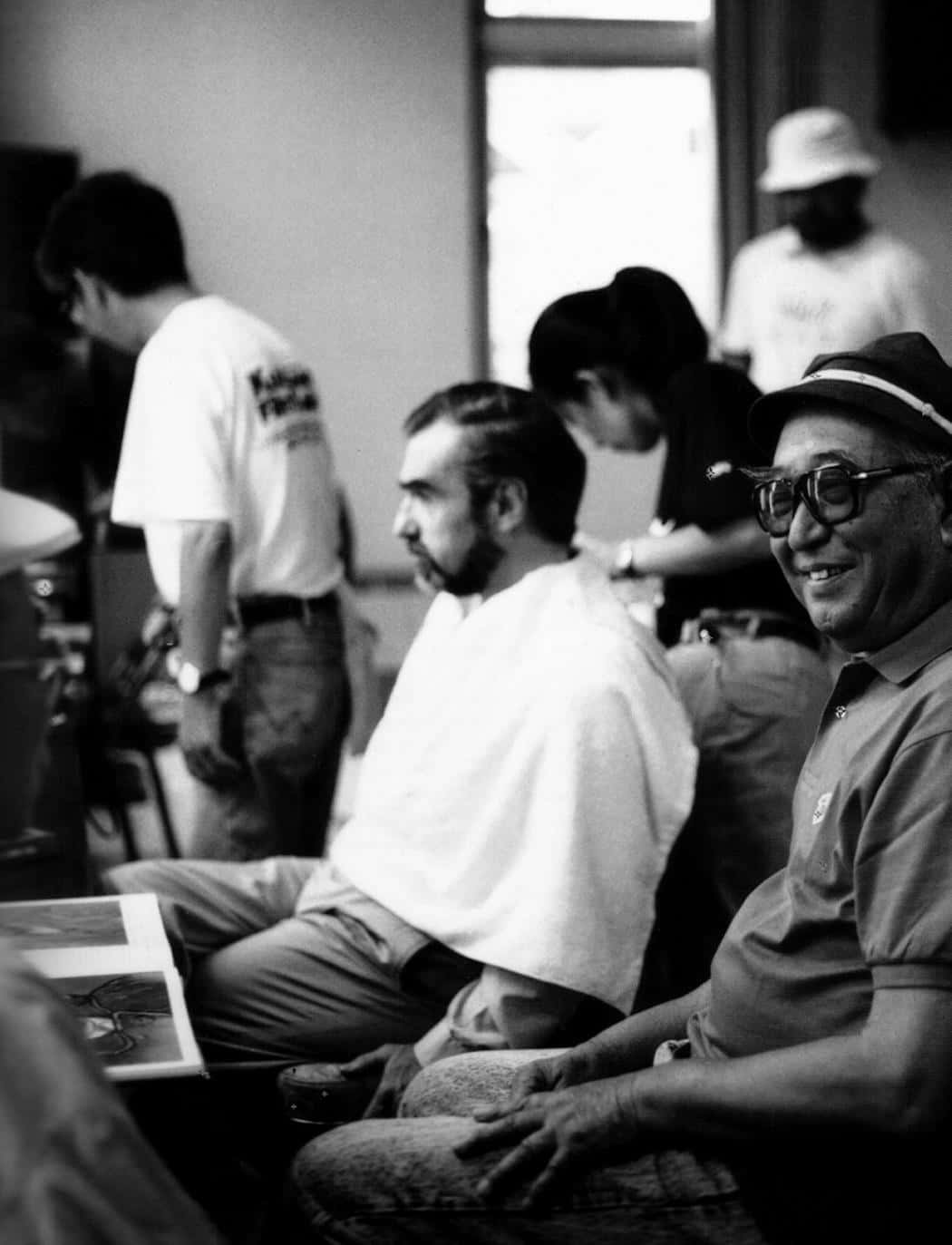 Akira Kurosawa 桌布 壁紙 — 黑白照片，一名戴帽子和眼鏡的微笑男子在休閒室內環境中坐在另一名男子旁邊。