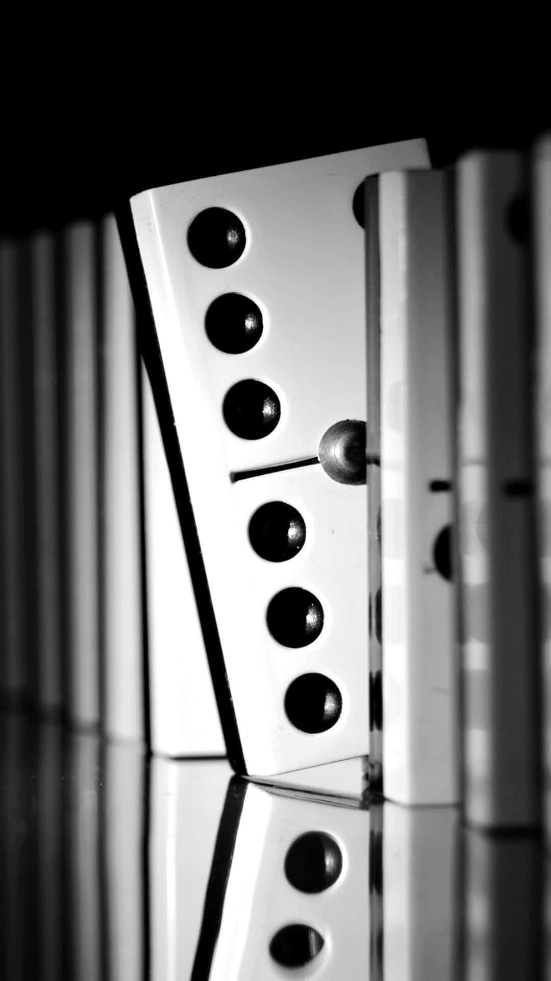 Domino 桌布 壁紙 — 黑白特寫，一排多米諾骨牌中有一塊正在反光表面上倒下。