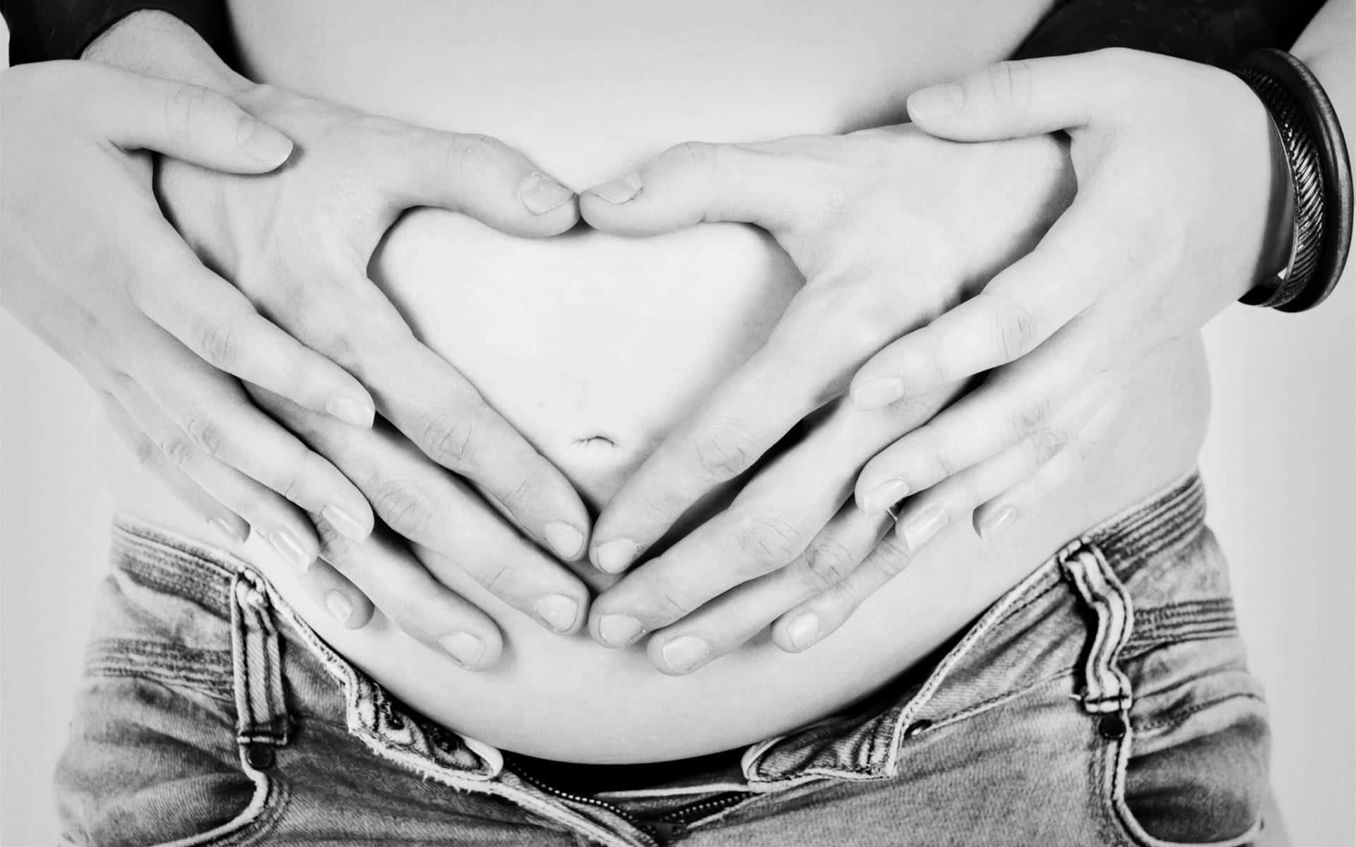 pregnancy 桌布 壁紙 — 黑白特寫鏡頭，雙手在裸露的腹部上形成心形，傳達愛與關懷。