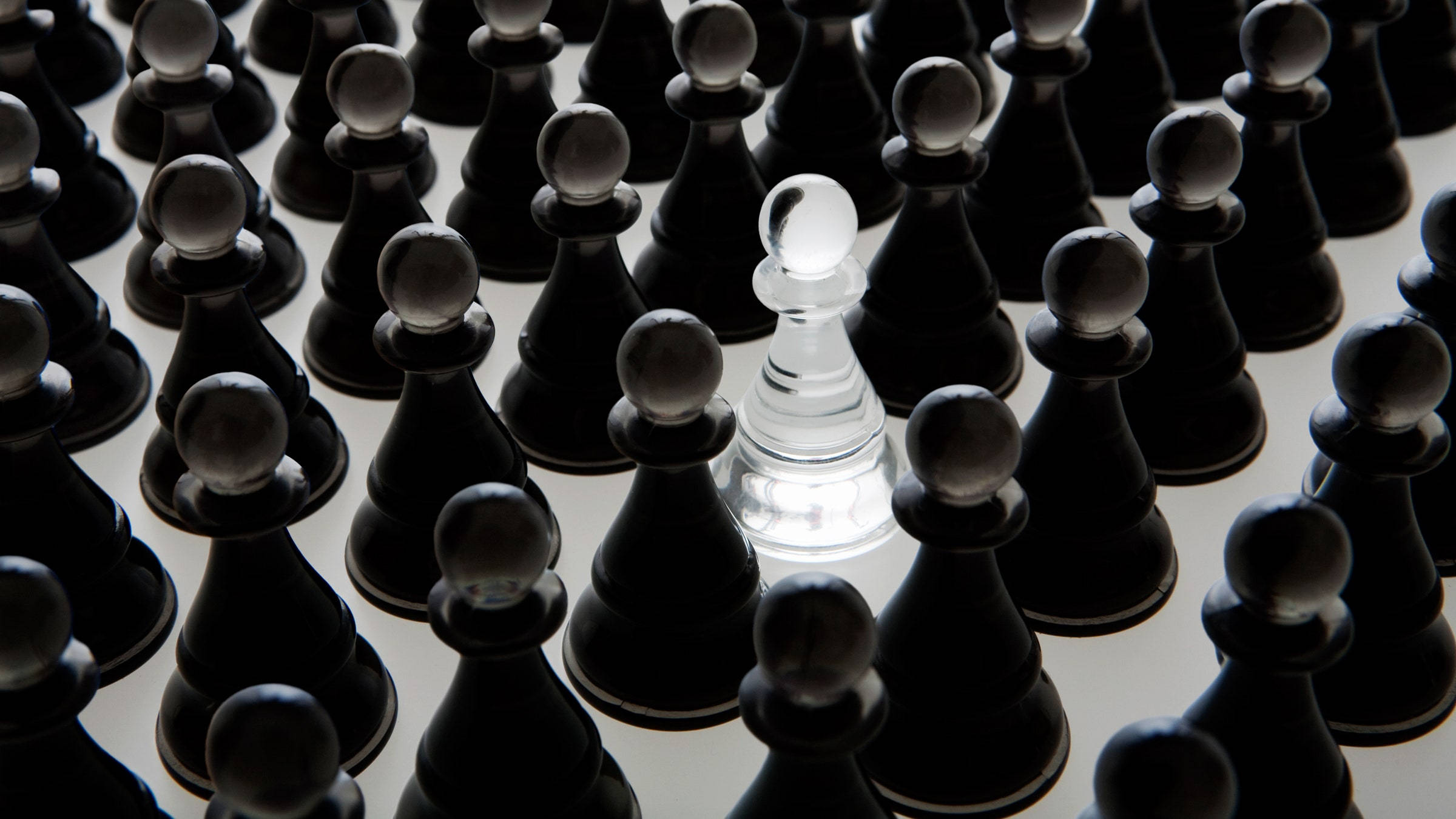 黑白玻璃棋子 壁紙 — 一個透明的國際象棋兵在淺色表面上的一片黑色兵海中脫穎而出。