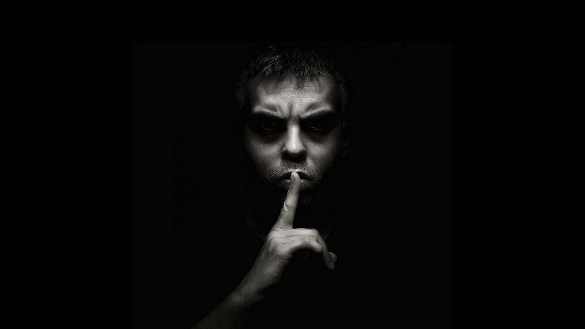 男人在黑暗的房間裏將手指放在嘴唇上，燈光戲劇性。