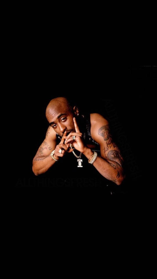 Tupac Shakur 在黑色背景前的攝影棚肖像，帶有紋身和珠寶。