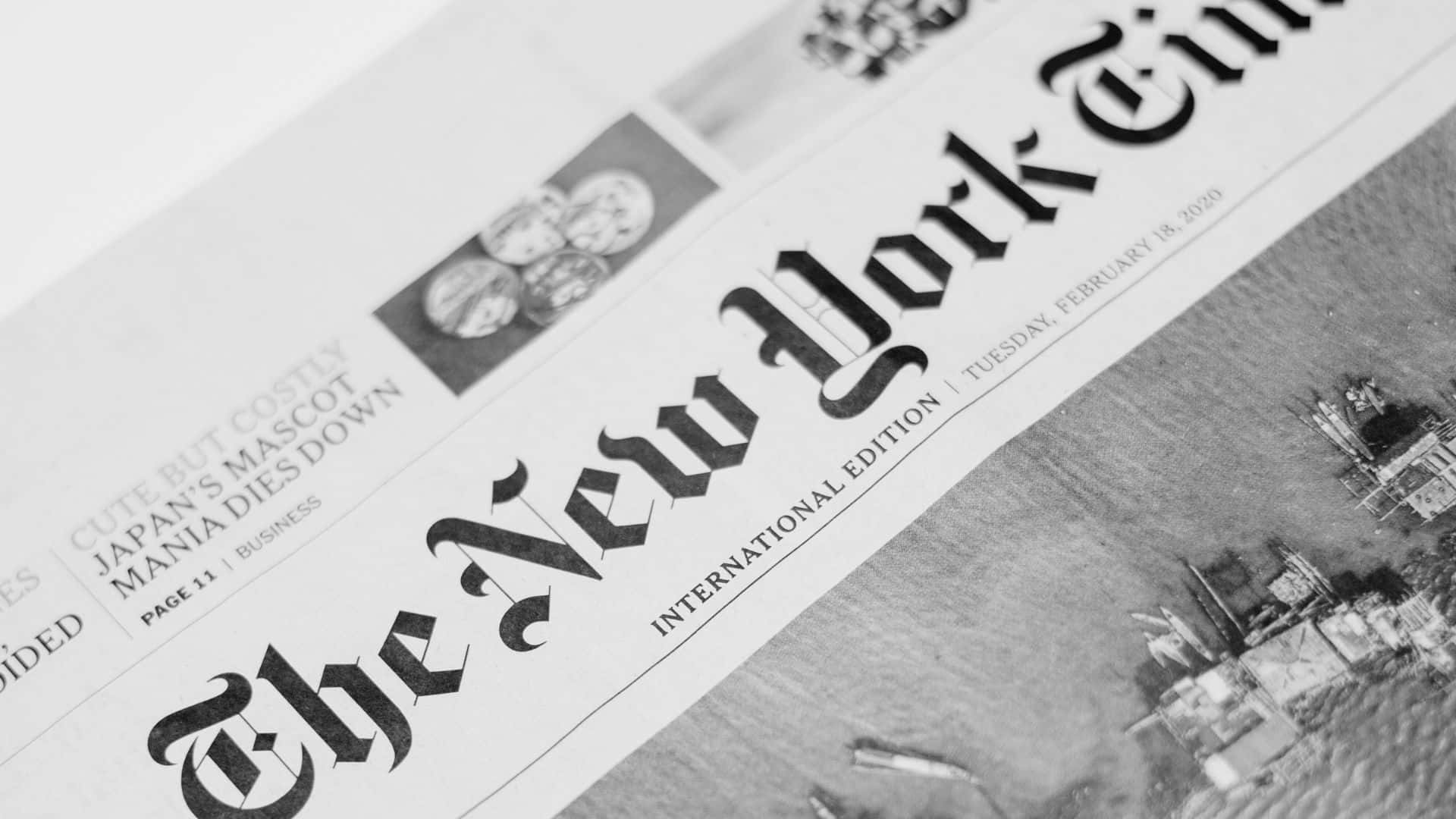 Black And White Newspaper 桌布 壁紙 — 黑白紐約時報報紙的特寫，包含城市景觀照片和關於日本吉祥物的標題。