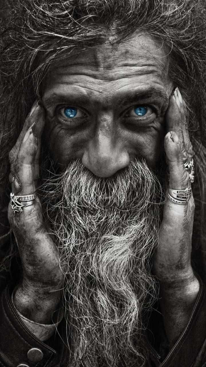 一個留鬍子的男人特寫，他有強烈的藍眼睛，用紋身的手托著臉。