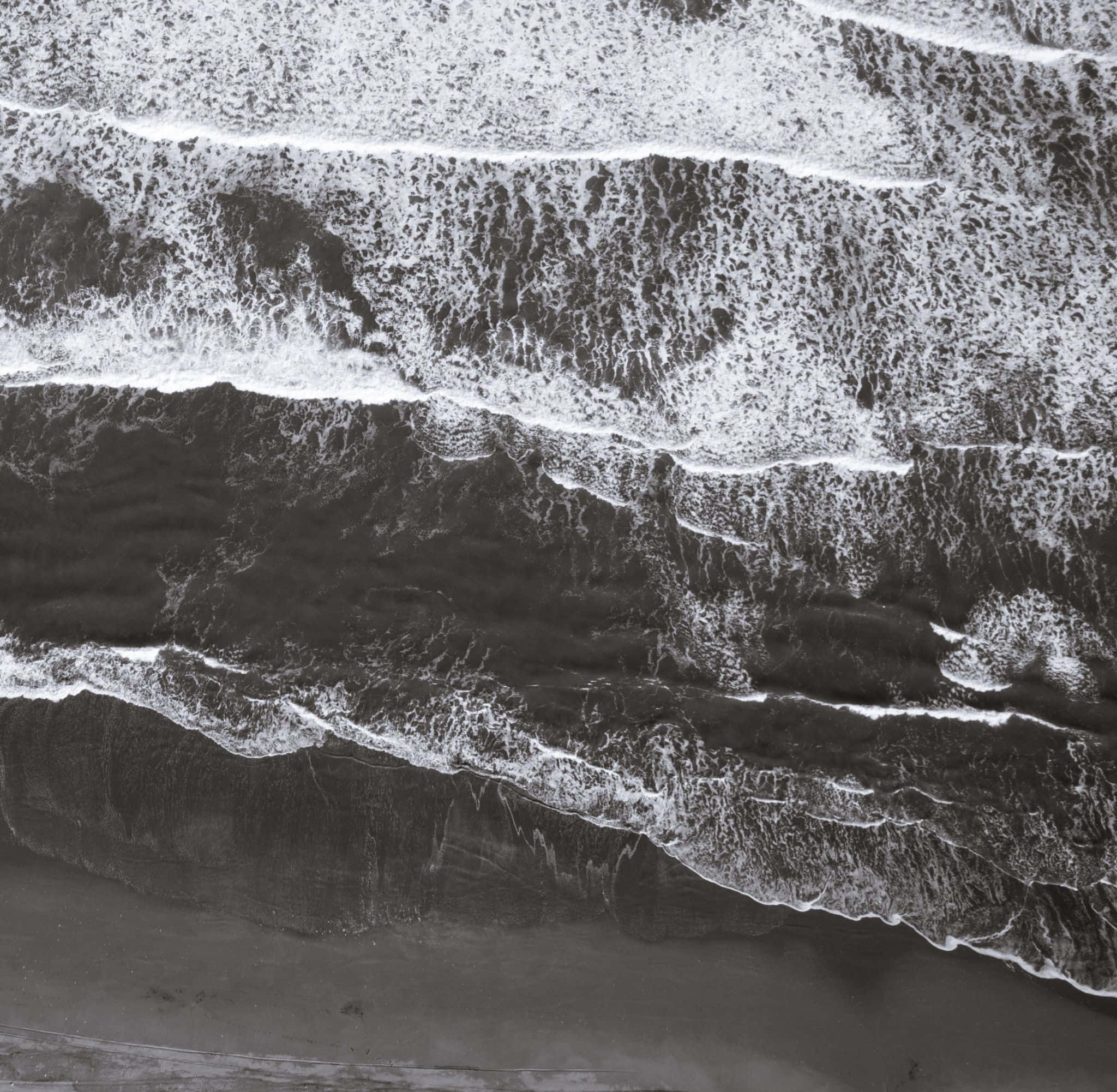 Black And White Beach 桌布 壁紙 — 黑白航空照片，展現有節奏的海浪以層疊圖案拍打深色沙灘。