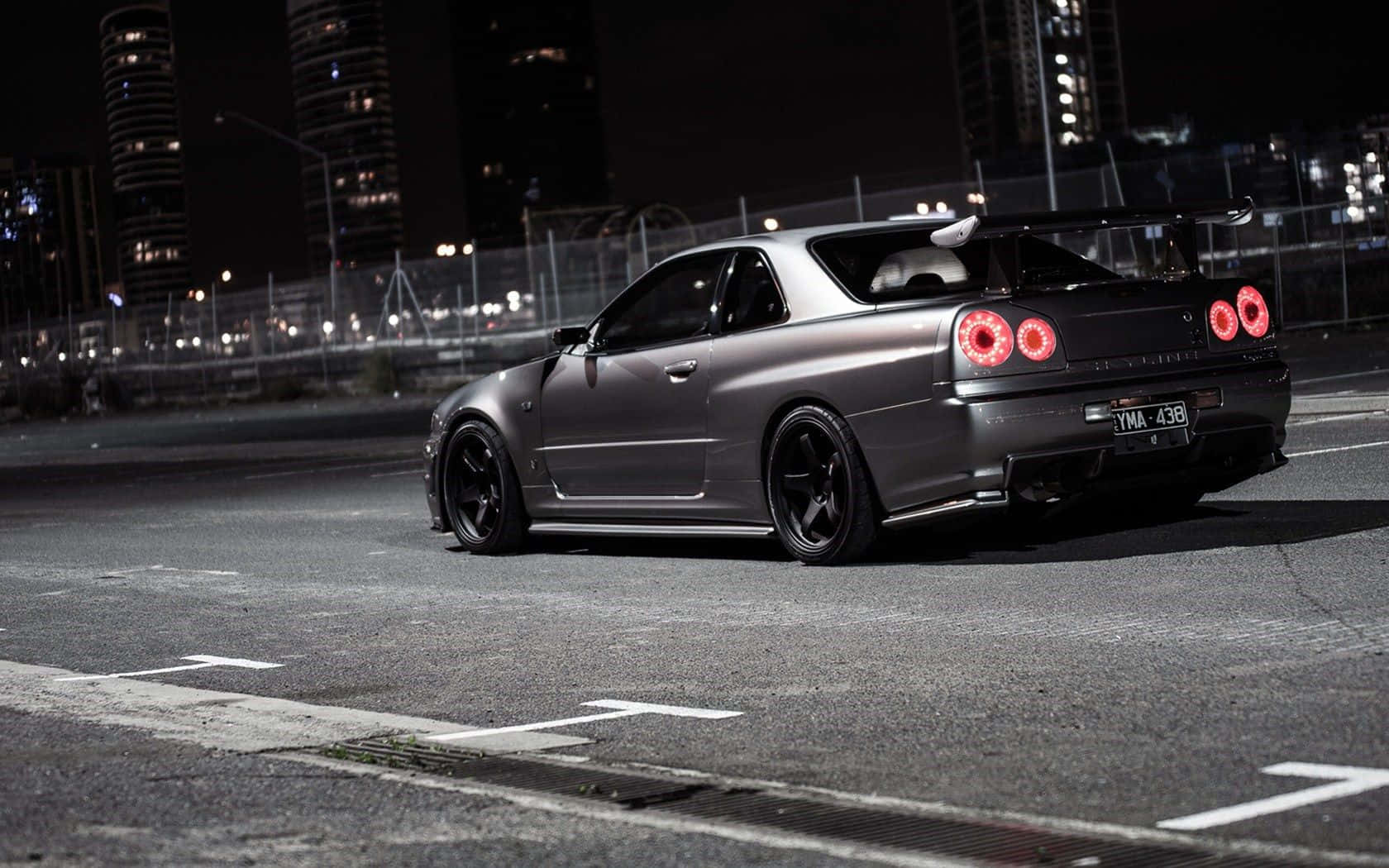 啞光灰色日產Skyline GT-R，紅色尾燈，夜晚停泊在城市街道上。