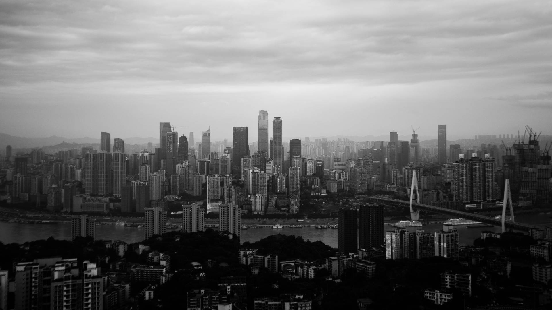 黑白重慶中國 壁紙 — 單色城市景觀，高聳的摩天大樓和河橋在陰天之下。