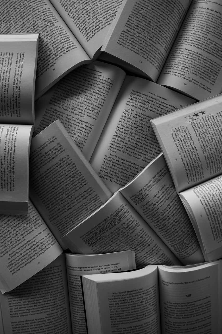 黑白開放書本的迷人影像 壁紙 — 單色俯視圖，散落的打開的書籍，可見的文字頁面，形成有紋理的文學拼貼。