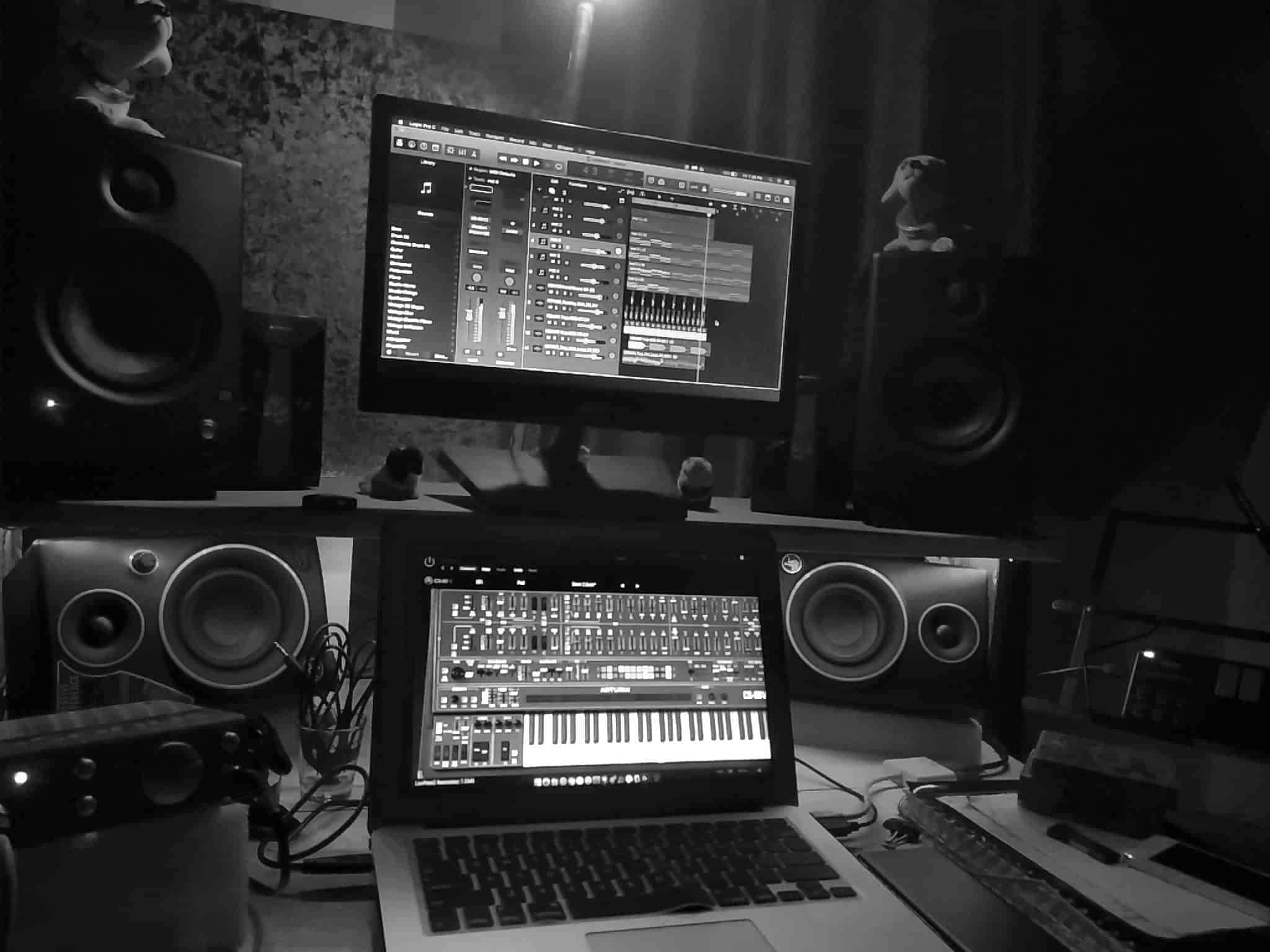 黑白風格 FL Studio 壁紙 — 一個單色家居工作室設置，發光的筆記型電腦和顯示器顯示音樂製作軟件，周圍環繞著揚聲器和人偶。