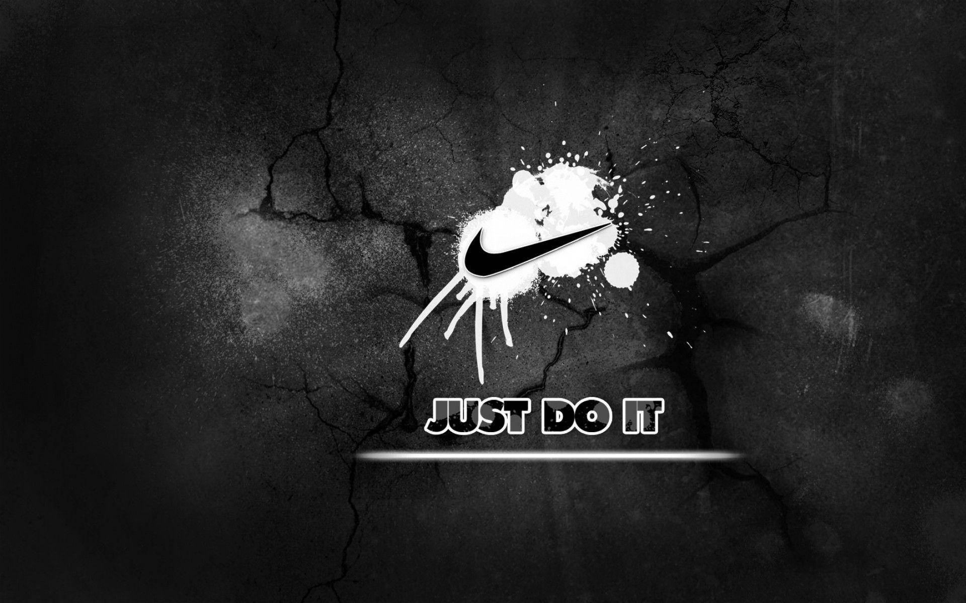 黑白風格「Just Do It」與裂紋石牆 壁紙 — 一個大膽的Nike剔號和「JUST DO IT」文字從白色油漆飛濺中迸發，背景是裂開的黑色混凝土牆。